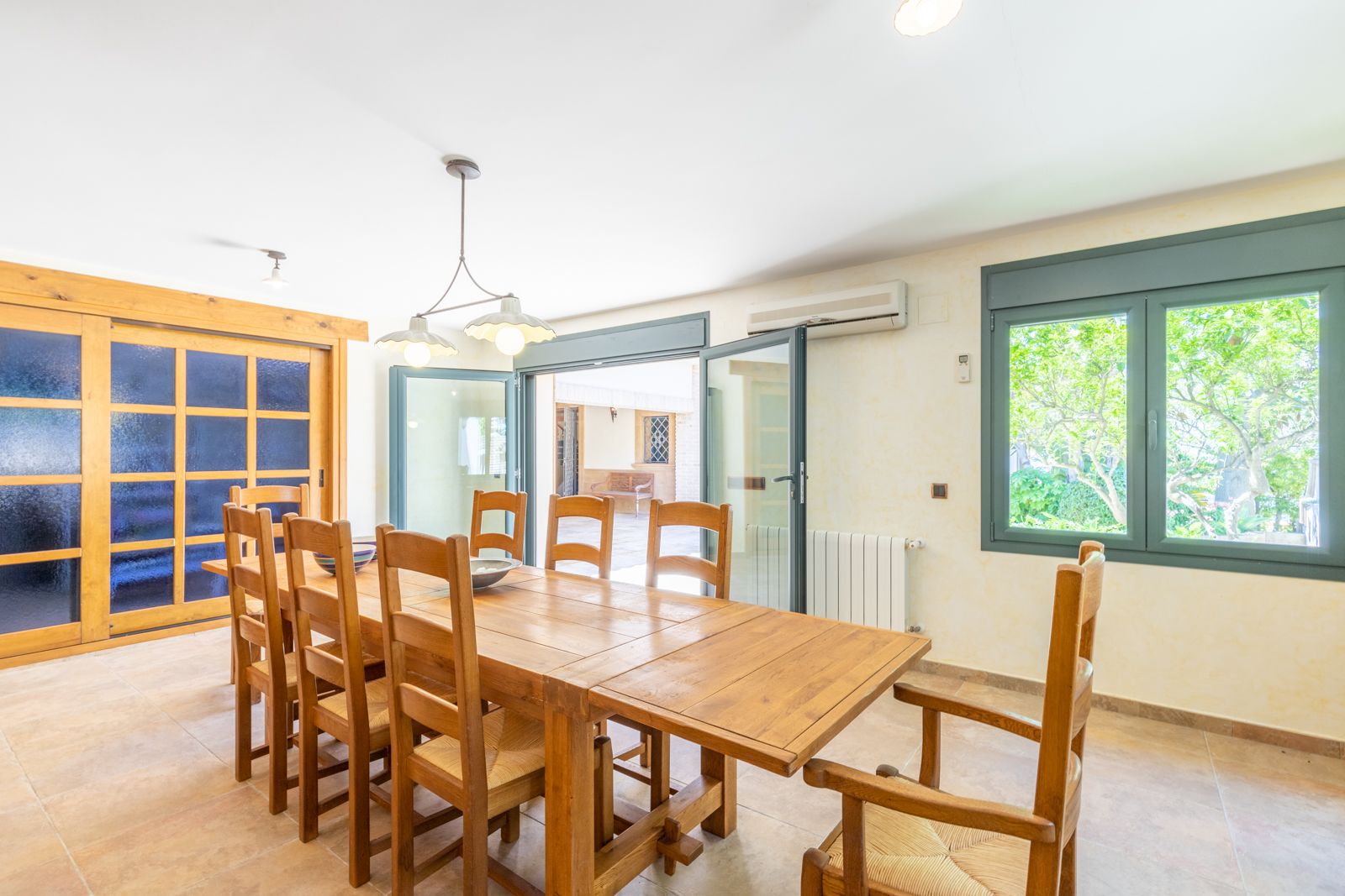 Salle à manger lumineuse avec table en bois massif et chaises assorties, accès terrasse et fenêtre donnant sur le jardin.