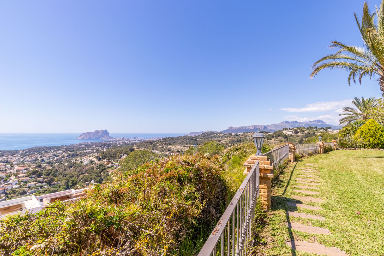 Vue panoramique depuis le jardin avec un chemin de pierre et une balustrade métallique.