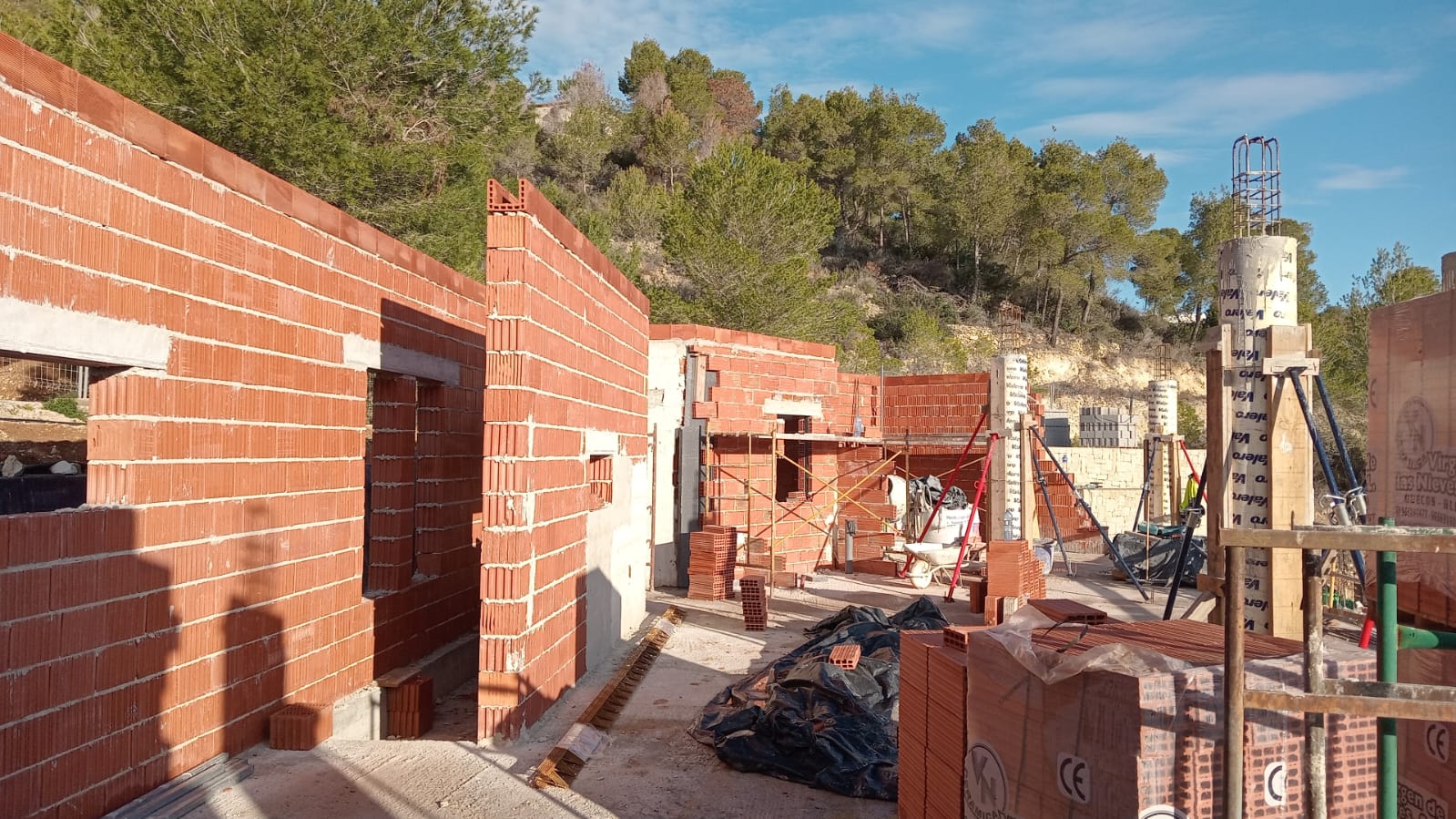 État actuel de la construction avec murs en briques thermo-argile et piliers en béton, entourés d'une forêt de pins méditerranéens.