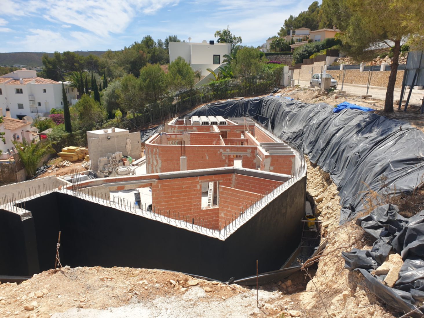 État actuel des travaux présentant la structure en briques et les murs de soutènement imperméabilisés sur un terrain en pente avec vue dégagée.