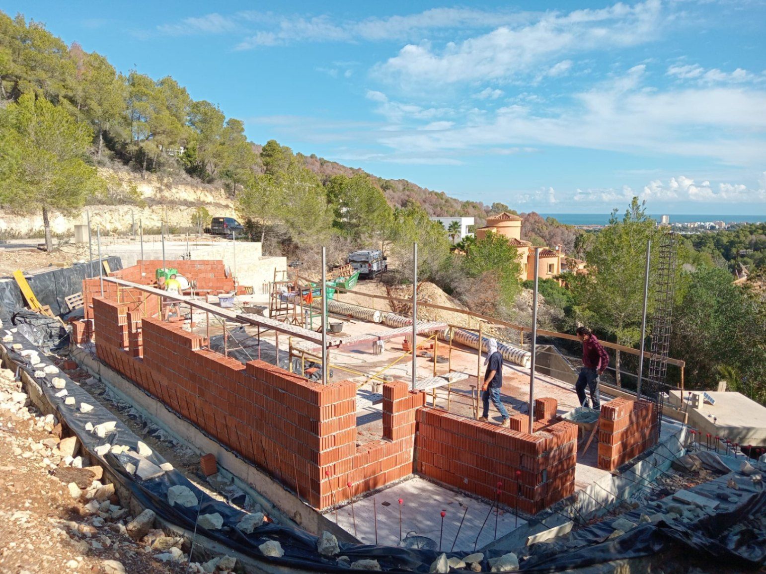 Phase initiale de construction de la villa à Jávea, montrant l'élévation des murs en briques sur les fondations avec une vue dégagée sur la mer Méditerranée.