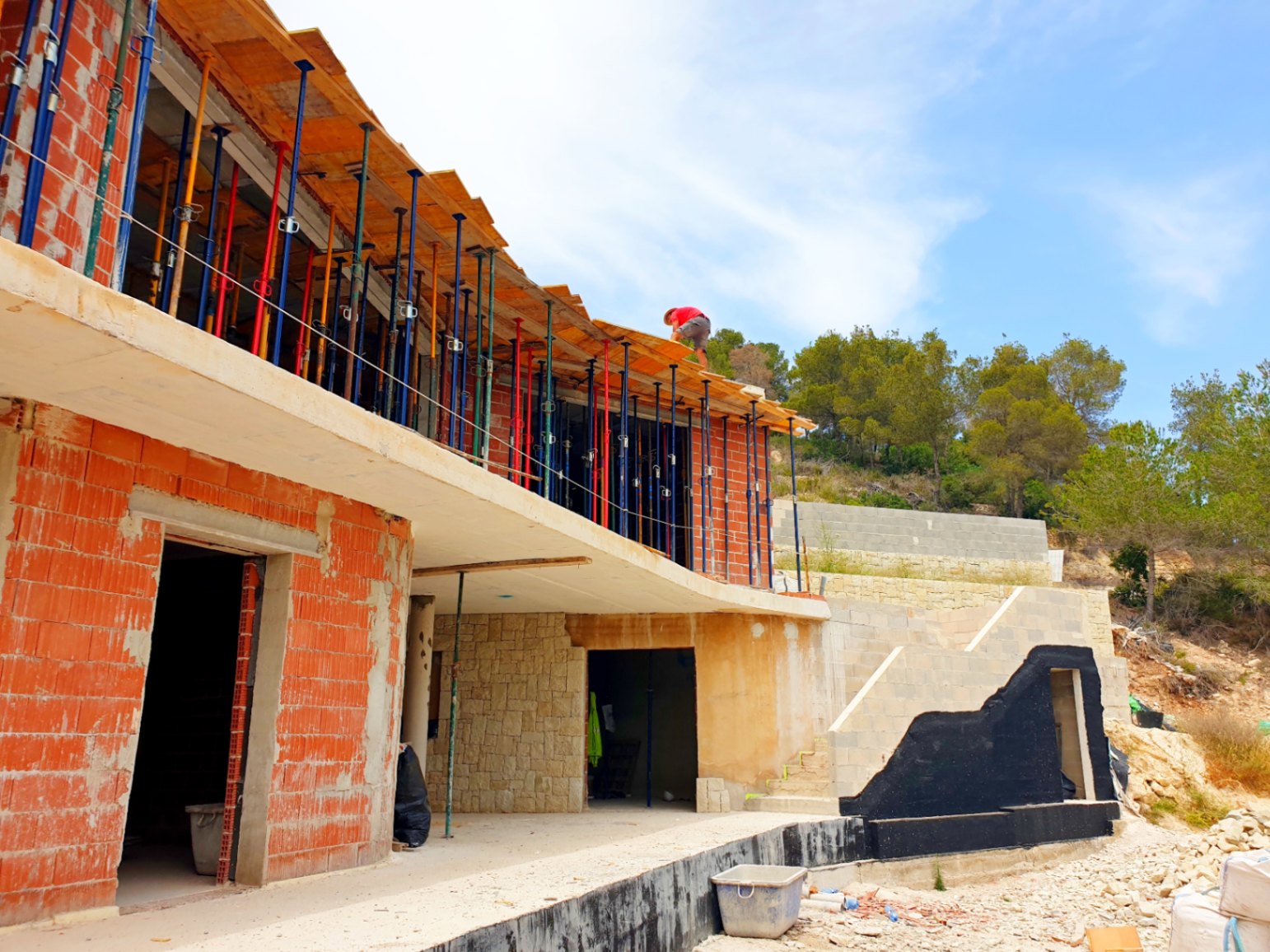 Vue extérieure de la phase de gros œuvre, illustrant la structure en briques, les murs en pierre naturelle et la dalle courbe de la terrasse.