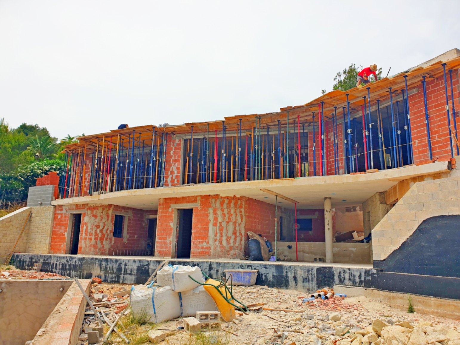 Vue extérieure de la villa en phase de gros œuvre, illustrant la structure en briques, les dalles en béton et les lignes courbes de l'étage supérieur.
