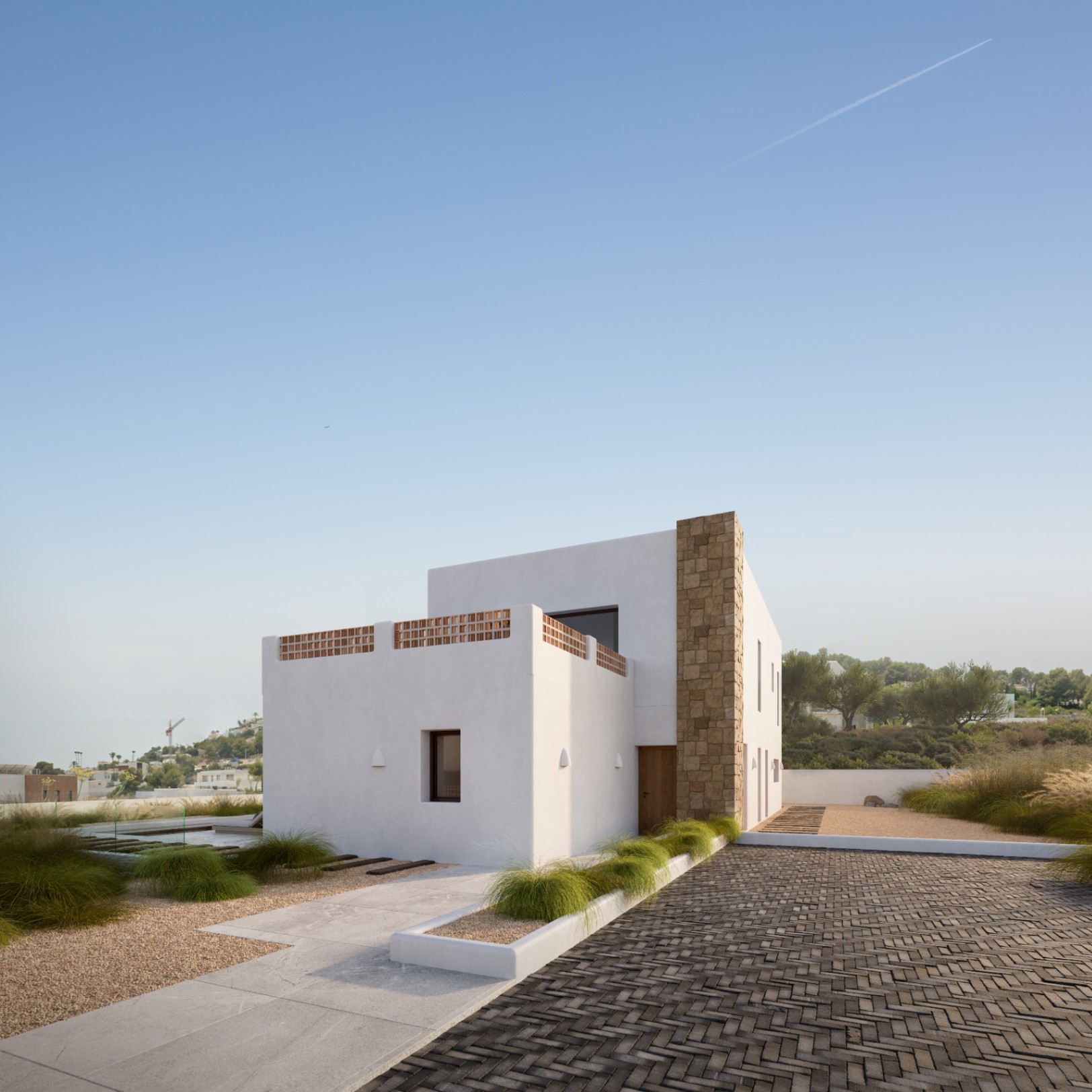 Façade méditerranéenne moderne avec murs blancs, pilier en pierre naturelle et terrasse à claustras en terre cuite, entourée d'un jardin minimaliste aux allées pavées.