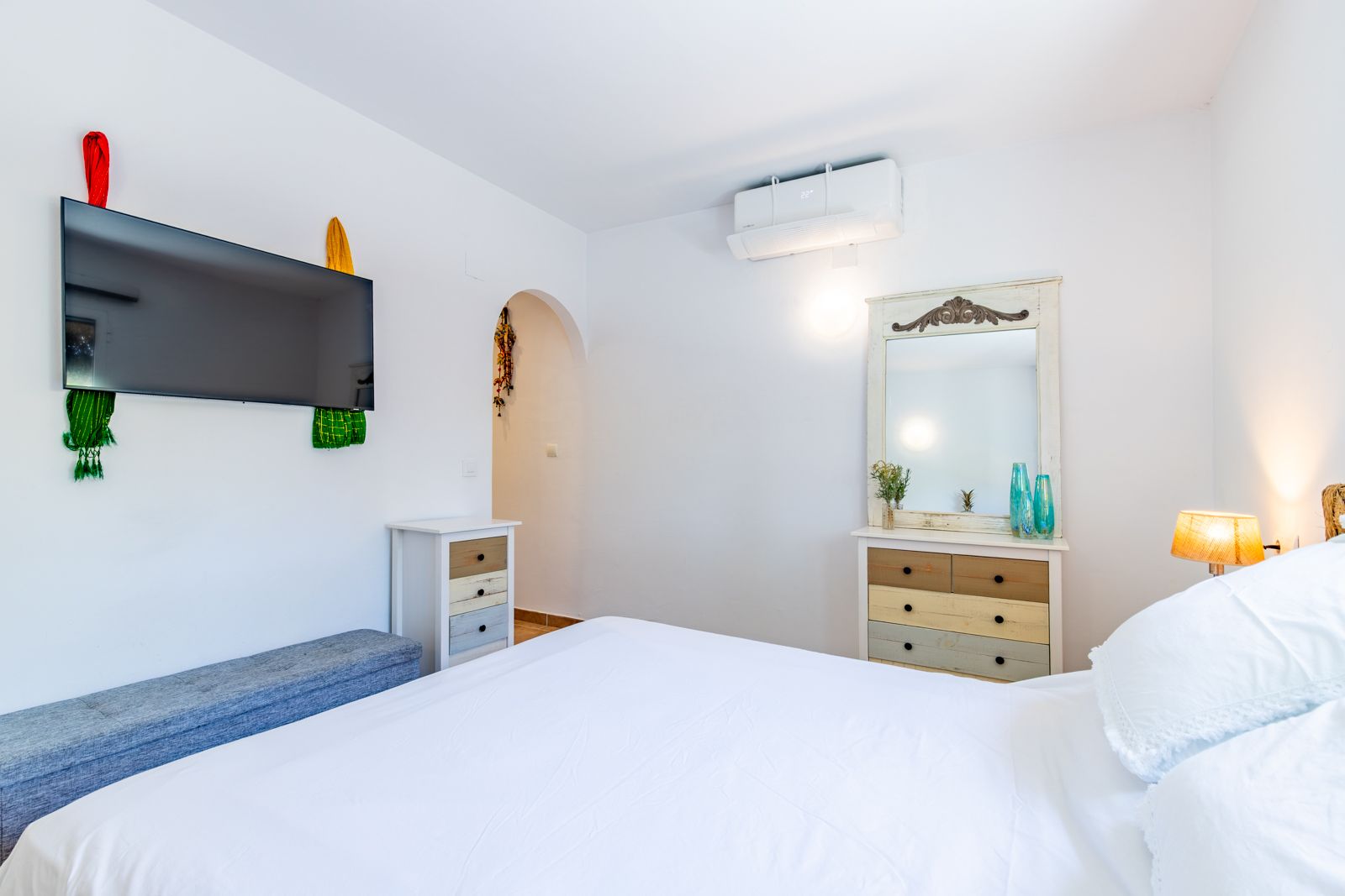 Chambre lumineuse avec lit double, commodes de style rustique, climatisation réversible et télévision murale dans un cadre épuré.
