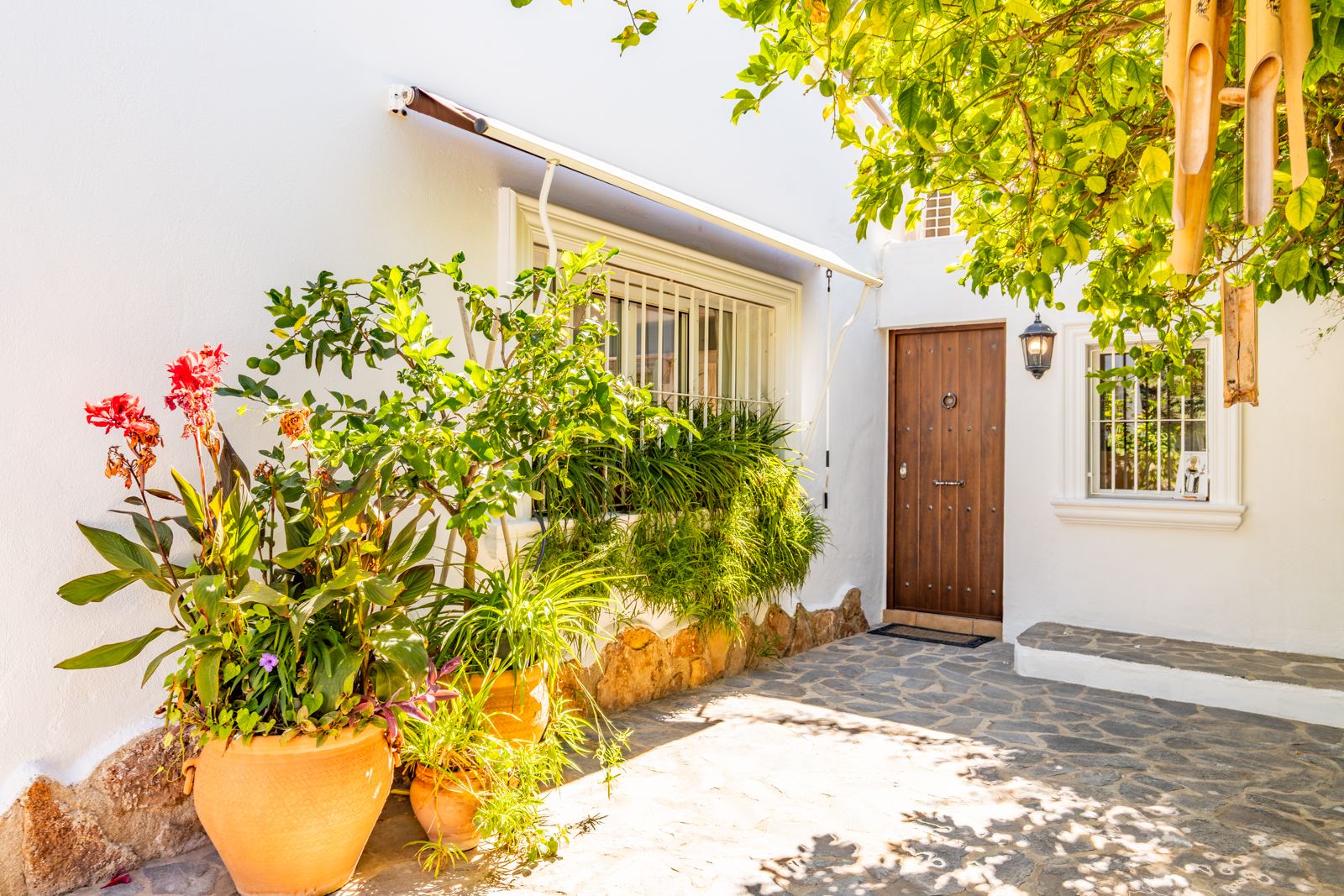 Entrée principale avec porte en bois rustique, pavage en pierre naturelle et pots en terre cuite sur une façade blanche traditionnelle.