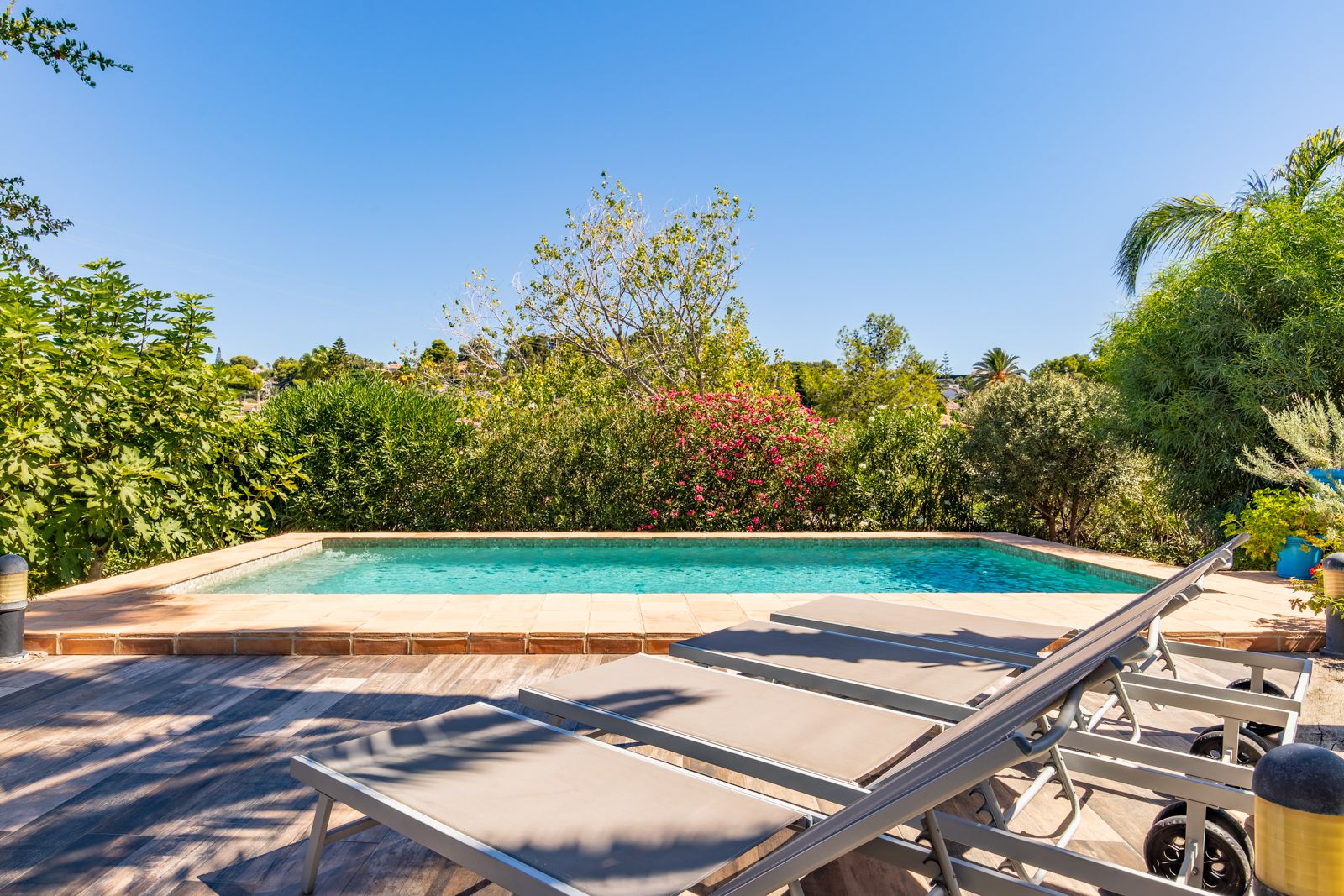 Espace piscine privée avec terrasse en grès cérame aspect bois, bains de soleil contemporains et végétation méditerranéenne dense.