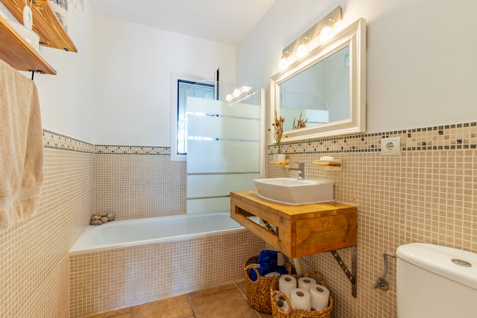 Salle de bain de style rustique avec un meuble sous-vasque en bois massif, une baignoire avec paroi en verre et un carrelage mural en mosaïque beige.