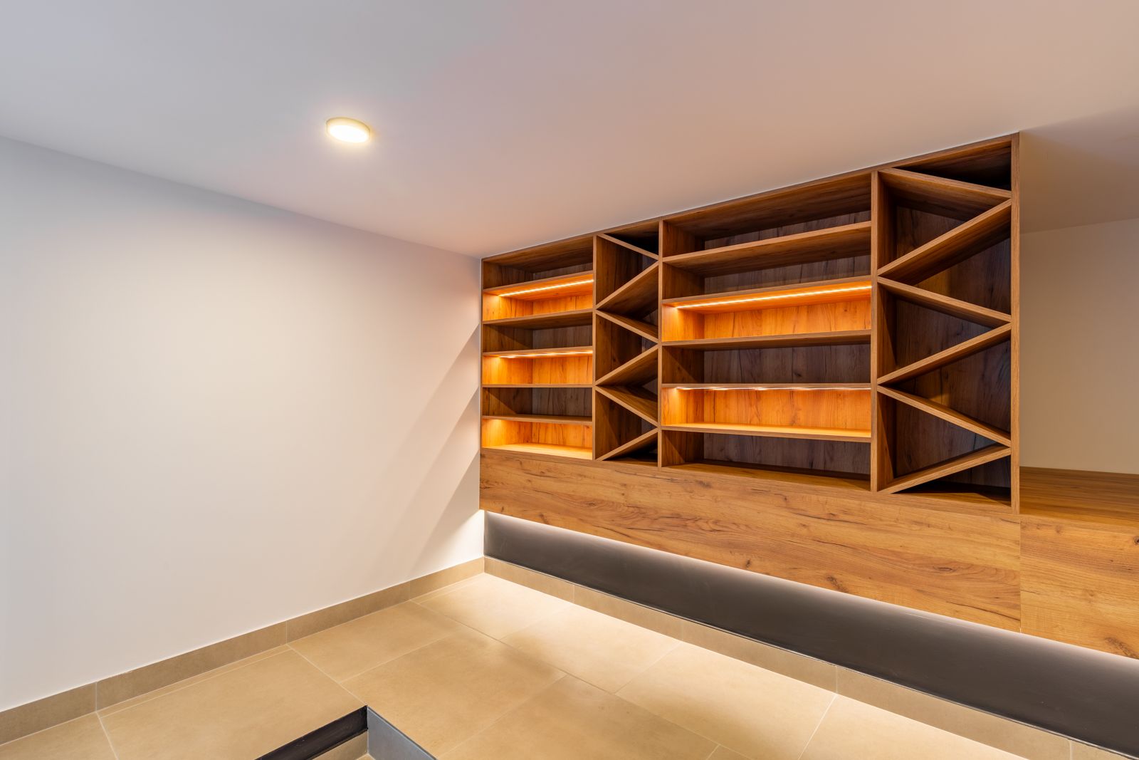 Cave à vin sur mesure en chêne avec éclairage LED intégré, étagères géométriques et sol en grès cérame de grand format.