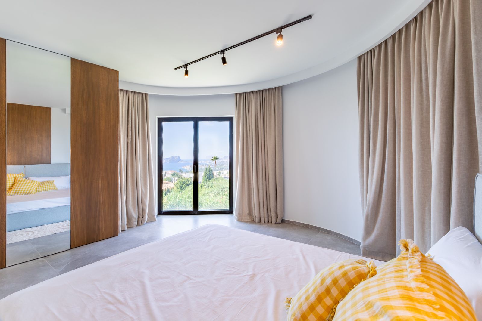 Chambre à coucher avec mur courbe, dressing sur mesure en chêne et accès direct à une terrasse offrant une vue dégagée sur la mer Méditerranée.