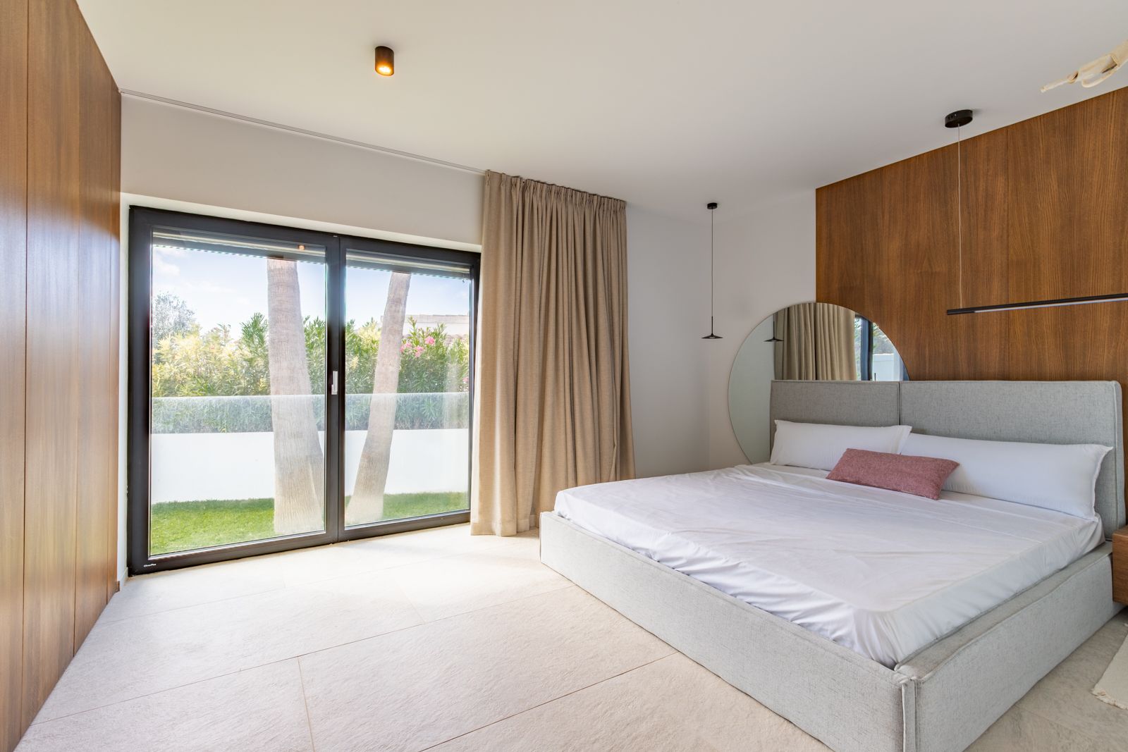 Chambre avec boiseries en chêne naturel, sol en grès cérame et accès direct au jardin par de larges baies vitrées à triple vitrage.