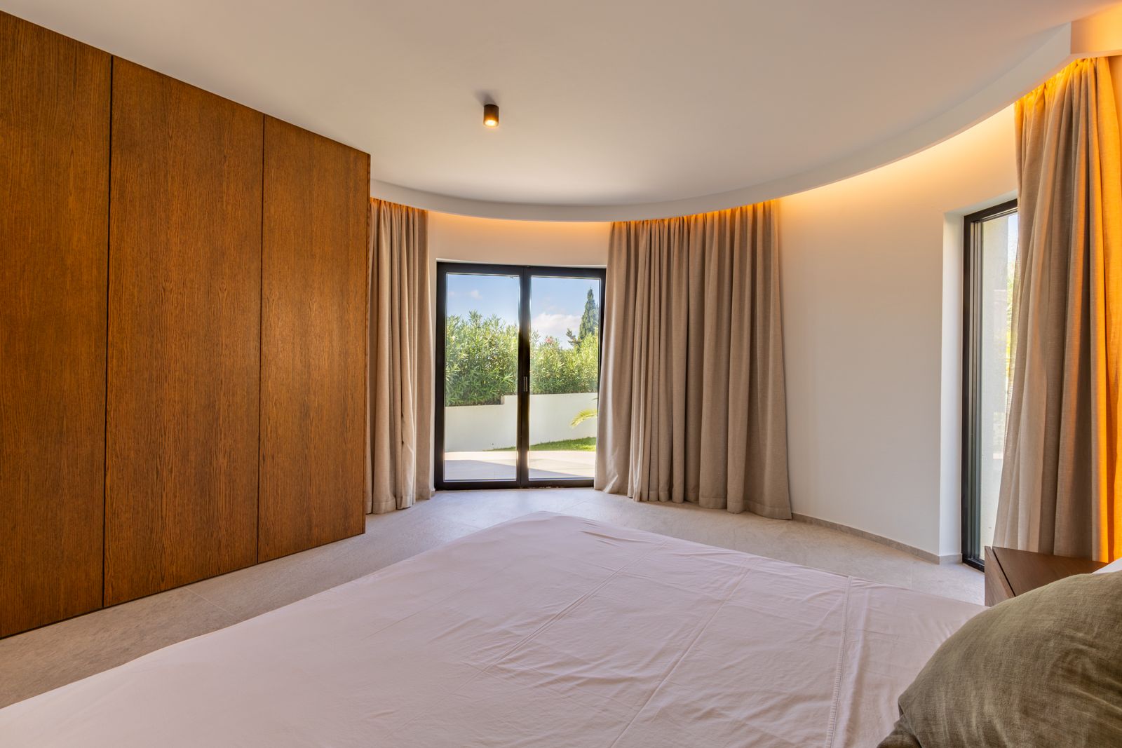 Chambre avec mur incurvé, rangements en chêne naturel et éclairage indirect. Les baies vitrées toute hauteur assurent une luminosité naturelle optimale.