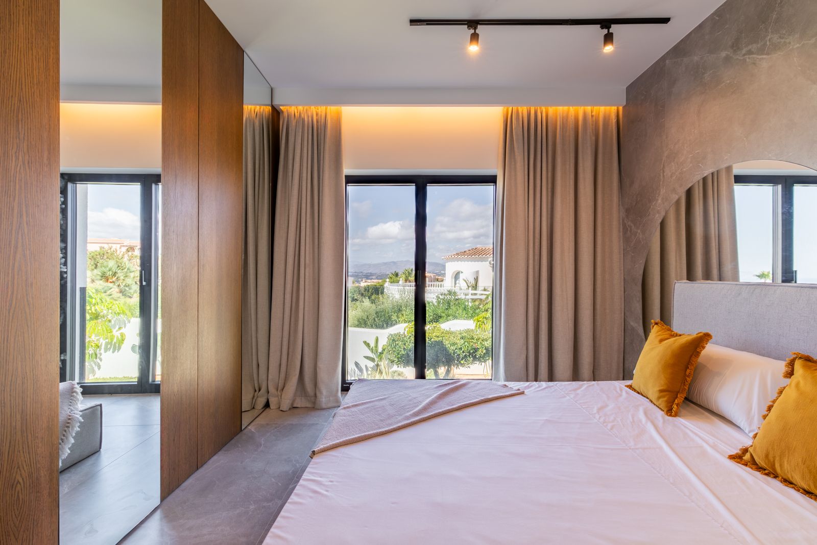Chambre avec panneaux en chêne naturel, sol en grès cérame et grandes baies vitrées offrant une vue sur le jardin et le paysage méditerranéen.