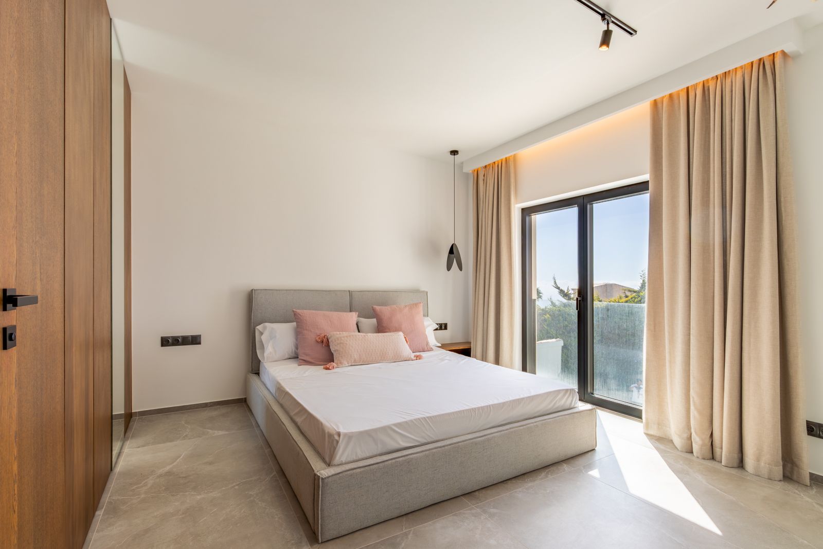 Chambre moderne avec sol en grès cérame, menuiserie en chêne sur mesure avec miroir intégré et accès direct à l'extérieur par de larges baies vitrées.
