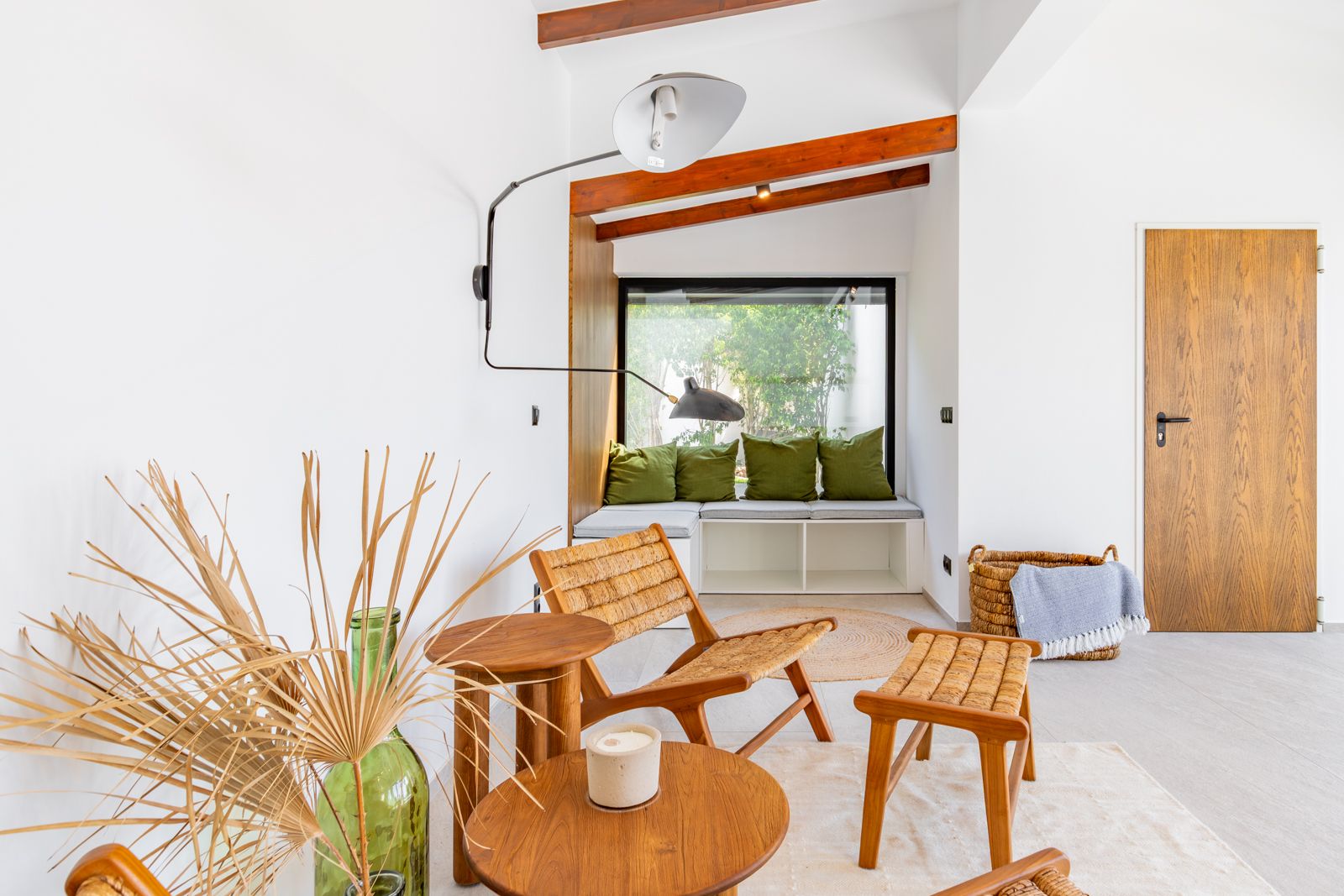 Coin lecture avec banquette intégrée sous une large fenêtre, poutres en bois apparentes et mobilier en fibres naturelles. Porte en chêne et luminaire mural design.