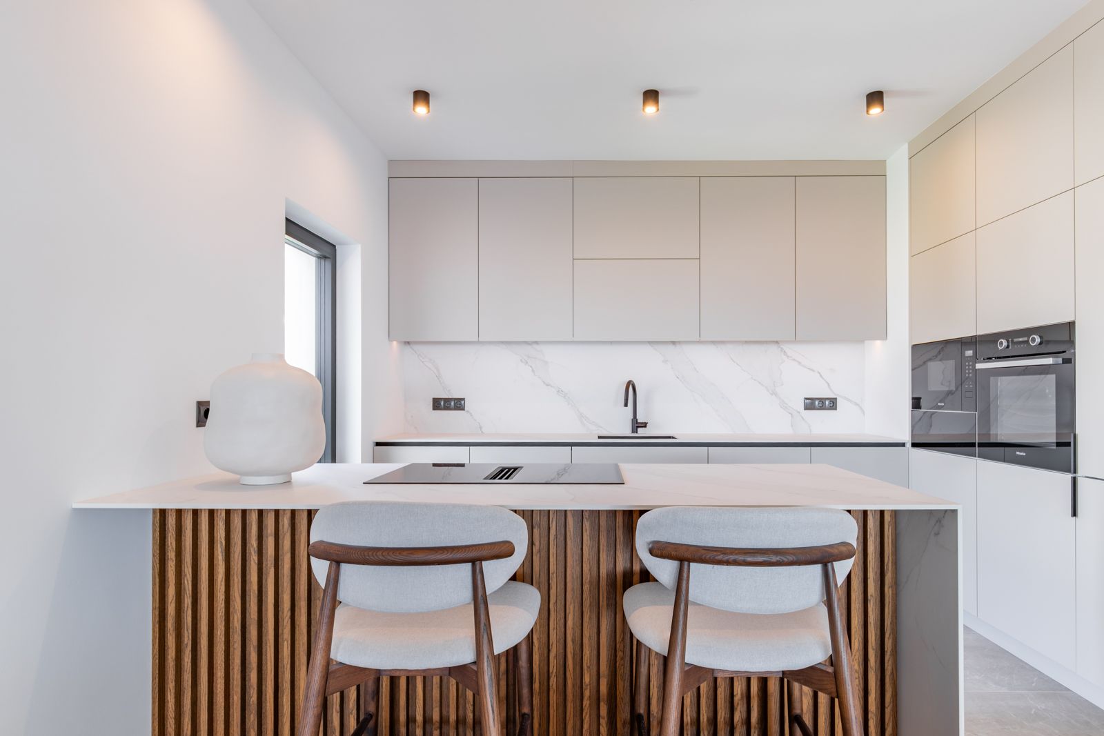 Cuisine de design avec îlot en lattes de chêne, plans de travail en pierre frittée et électroménagers Miele intégrés dans un mobilier minimaliste épuré.