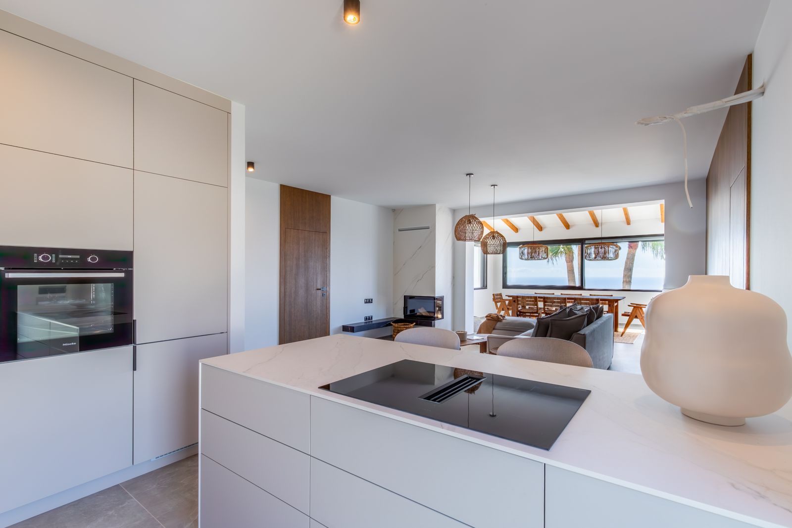 Cuisine ouverte avec îlot en pierre frittée, plaque à induction intégrée et four Miele, s'ouvrant sur un salon lumineux avec vue panoramique sur la mer.