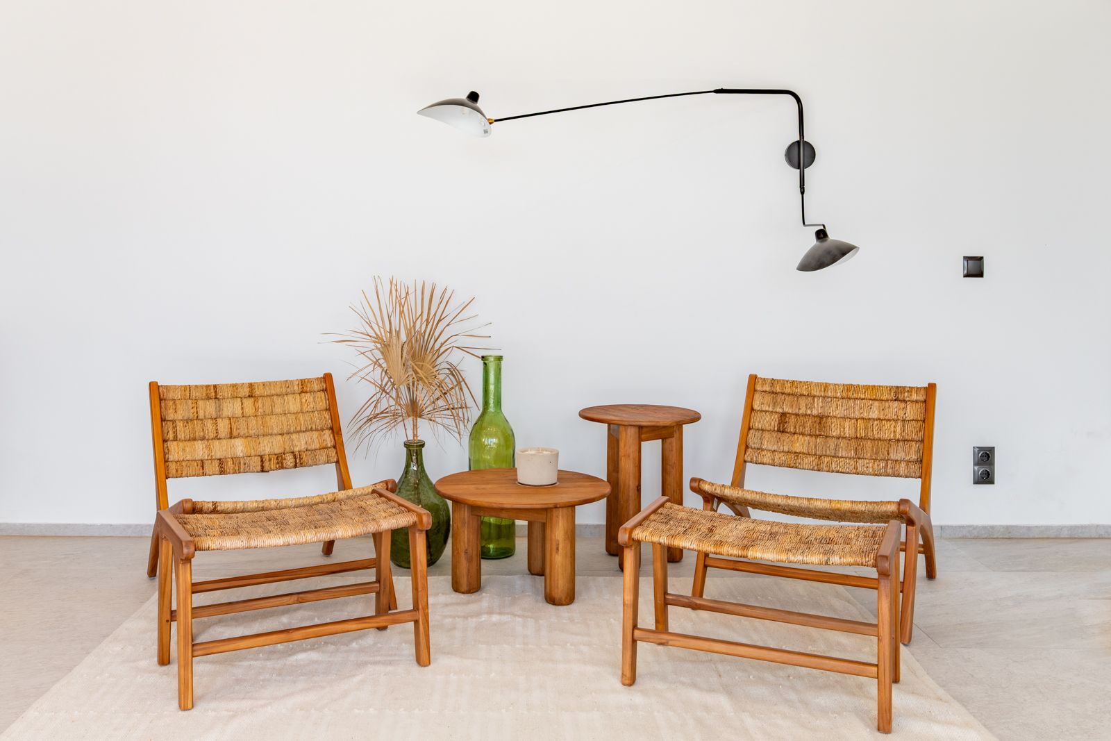 Espace de détente avec fauteuils en bois et fibres naturelles, tables en teck et applique murale noire orientable sur un sol en grès cérame clair.