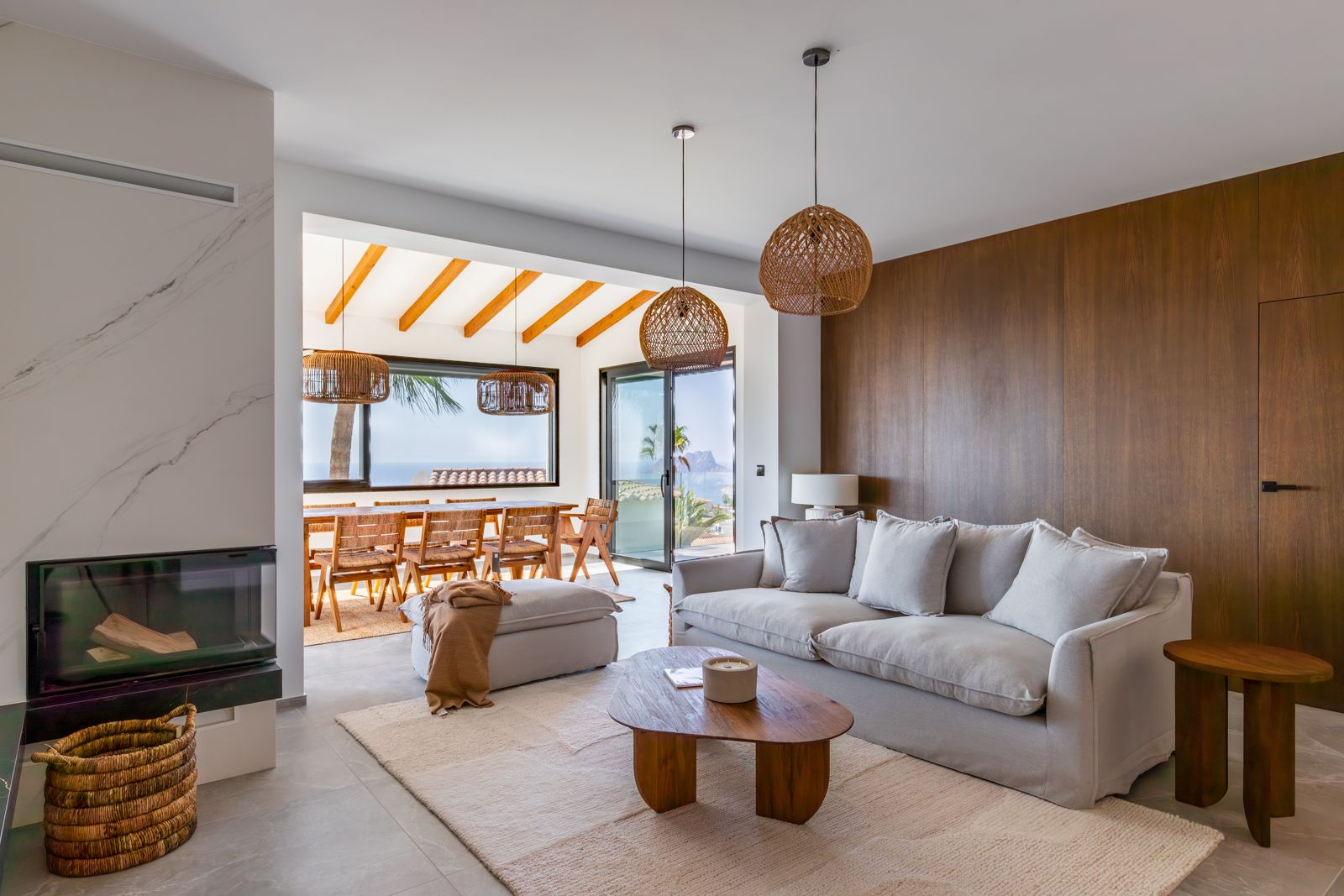 Espace de vie avec cheminée intégrée, mur en chêne naturel et vue mer. Décoré de suspensions en fibres et d'un coin repas avec poutres apparentes en bois massif.