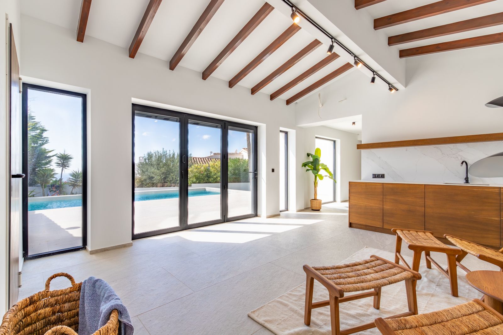 Espace de vie lumineux avec poutres apparentes, sol en grès cérame et larges baies vitrées s'ouvrant sur la terrasse et la piscine.