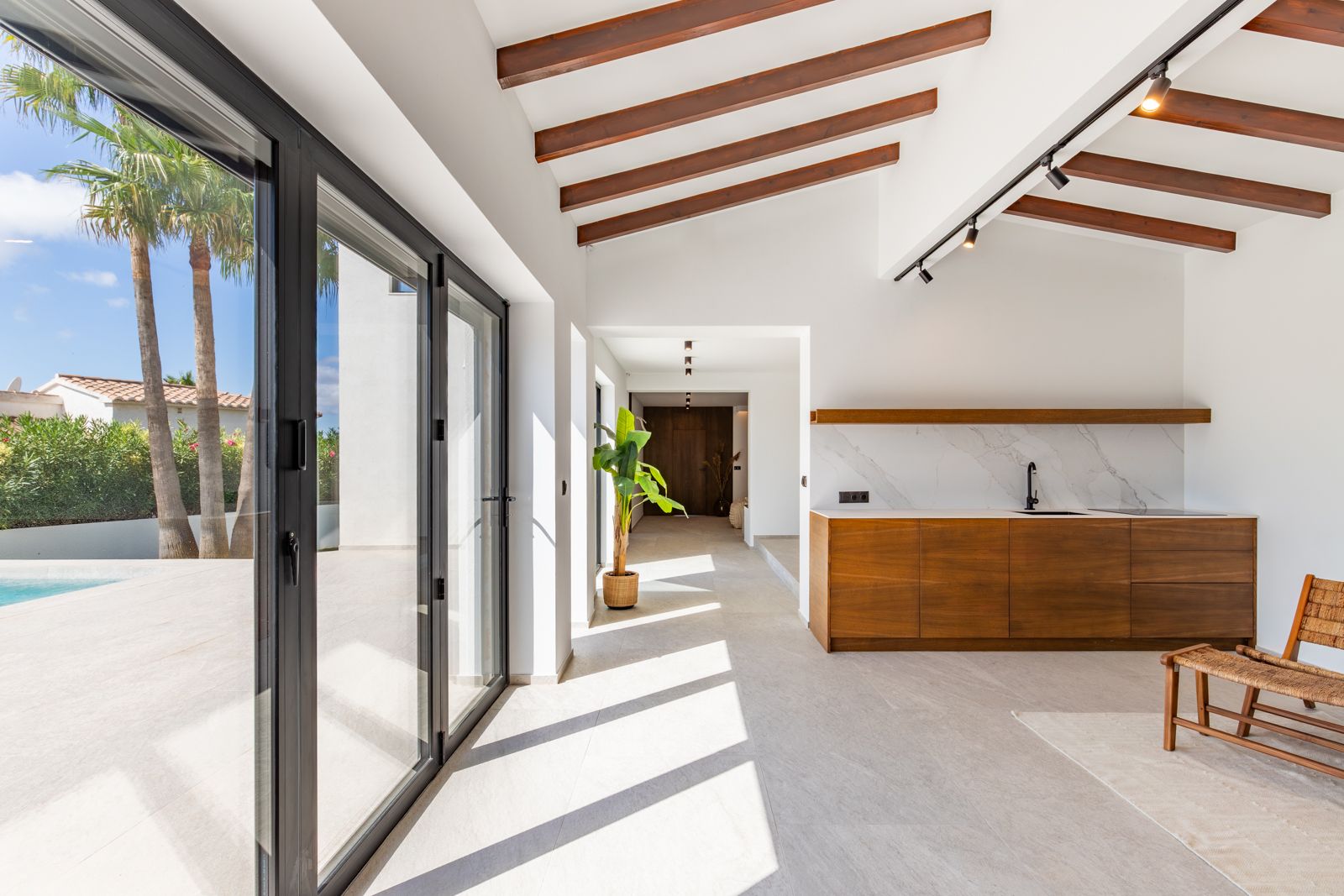 Espace de vie ouvert avec poutres apparentes, kitchenette en chêne massif et grandes baies vitrées créant une transition fluide vers la terrasse et la piscine.