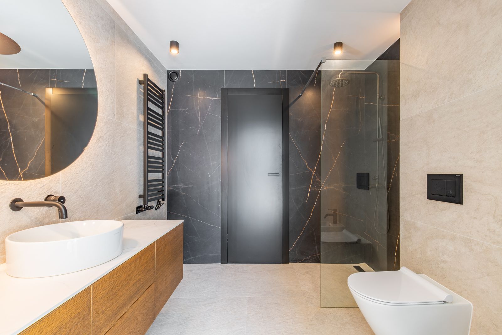 Salle de bains design avec grès cérame grand format, miroir rétroéclairé, meuble vasque en bois et douche à l'italienne avec robinetterie noire mate.