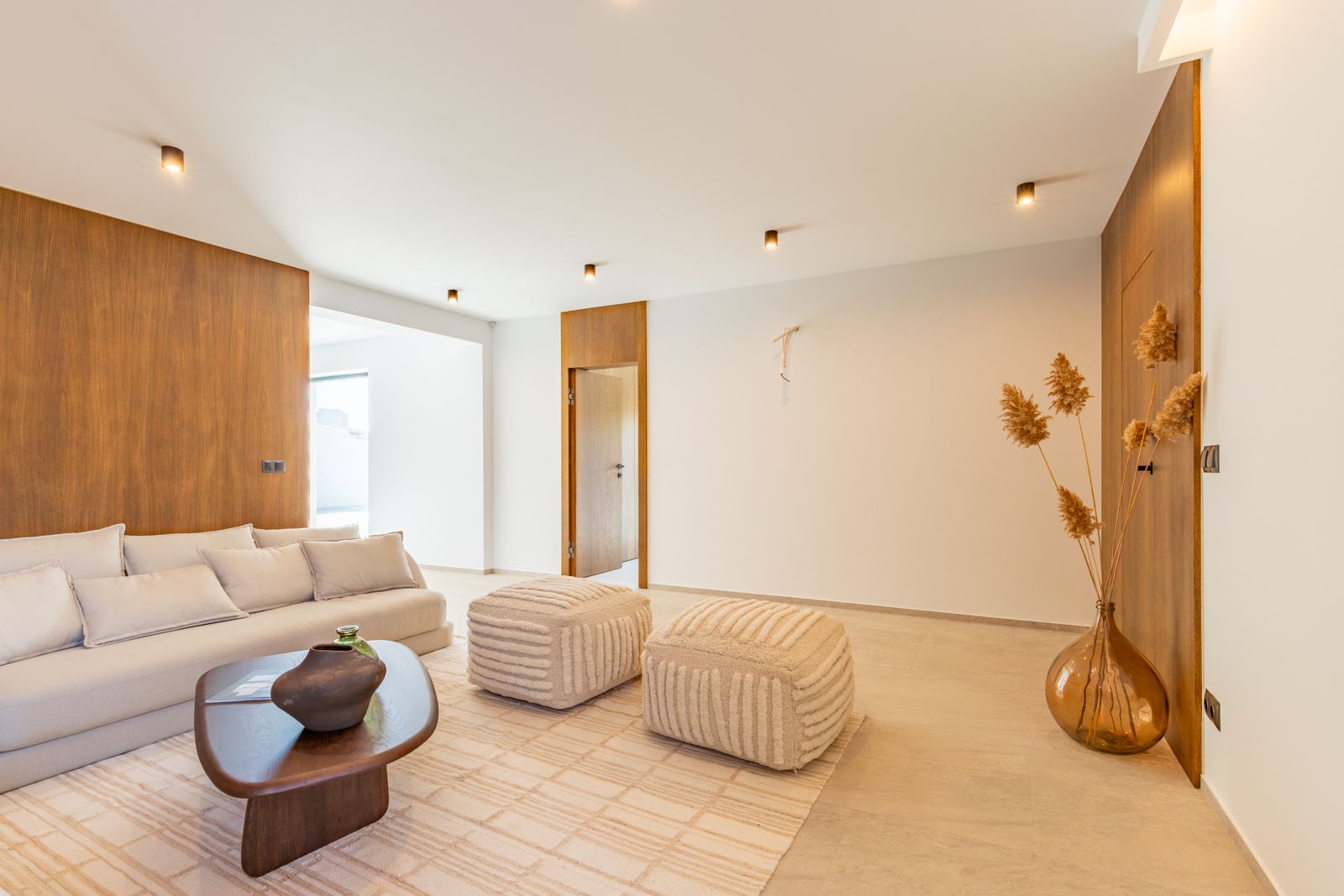 Salon minimaliste avec panneaux muraux en chêne naturel, sol en grès cérame grand format et mobilier design éclairé par des spots de plafond encastrés.