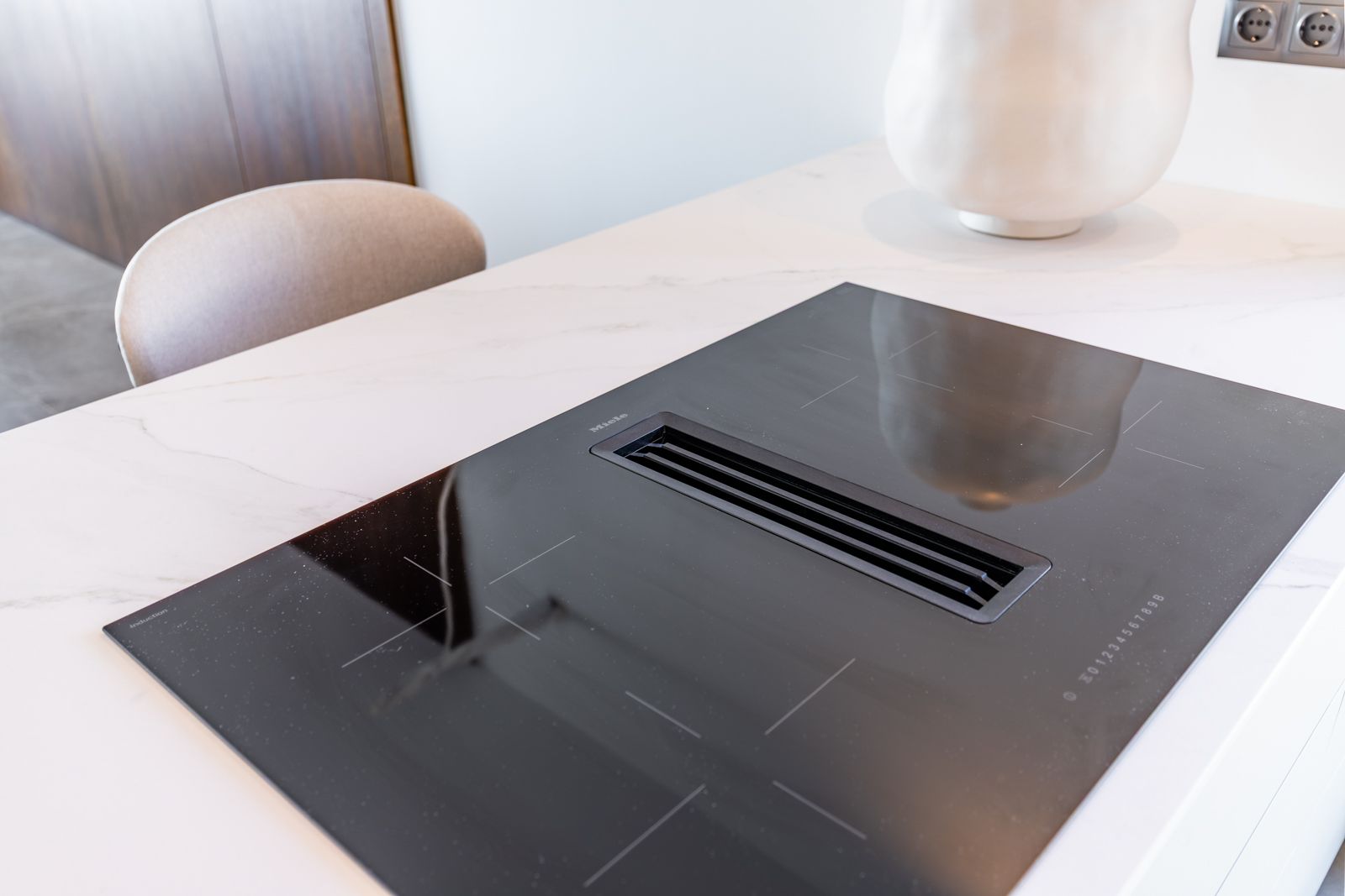 Table de cuisson à induction Miele avec hotte intégrée sur un plan de travail en pierre frittée blanche veinée.