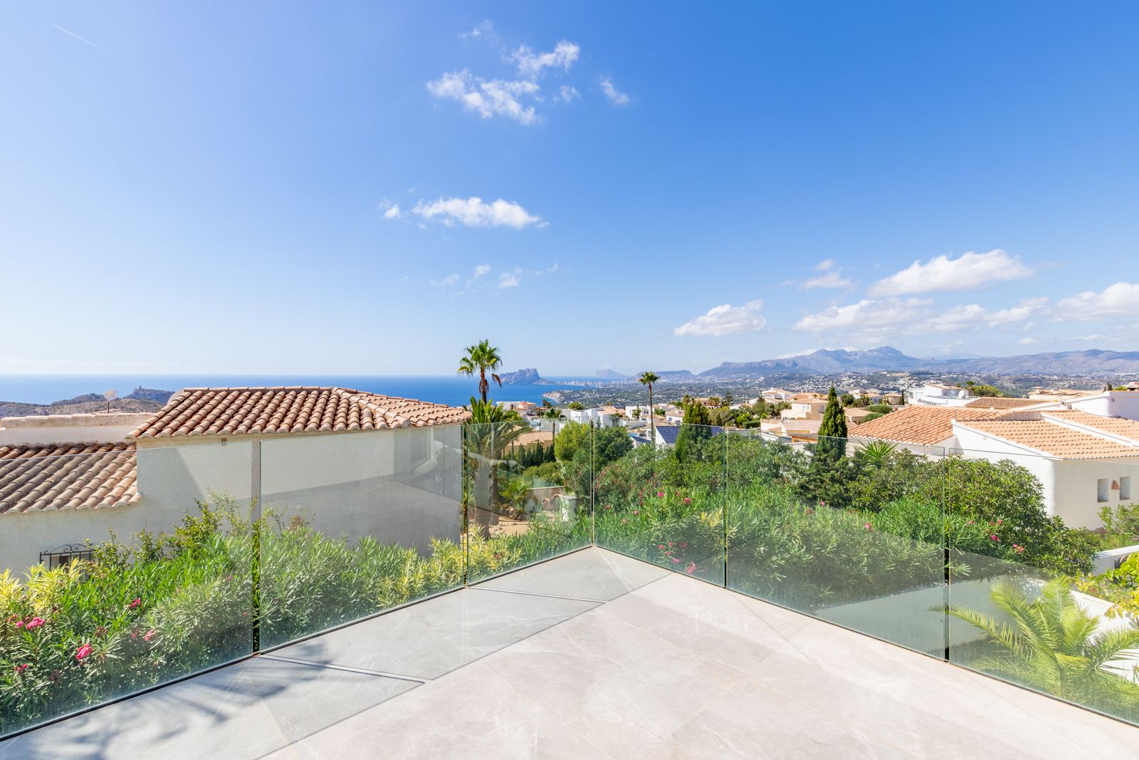 Terrasse supérieure avec sol en grès cérame et garde-corps en verre, offrant une vue panoramique sur la mer Méditerranée et le Peñón de Ifach.