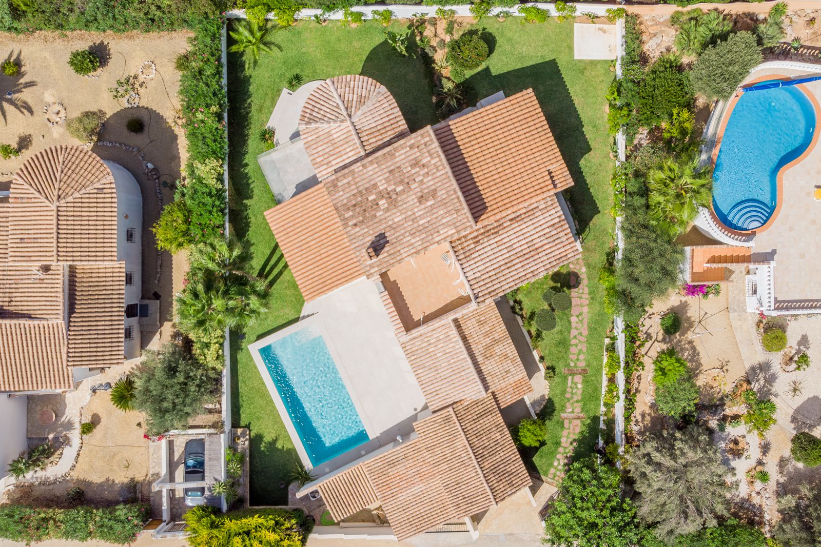 Vue aérienne de la villa révélant la toiture en tuiles, la piscine rectangulaire et le jardin paysager avec sa pelouse impeccable et ses haies.
