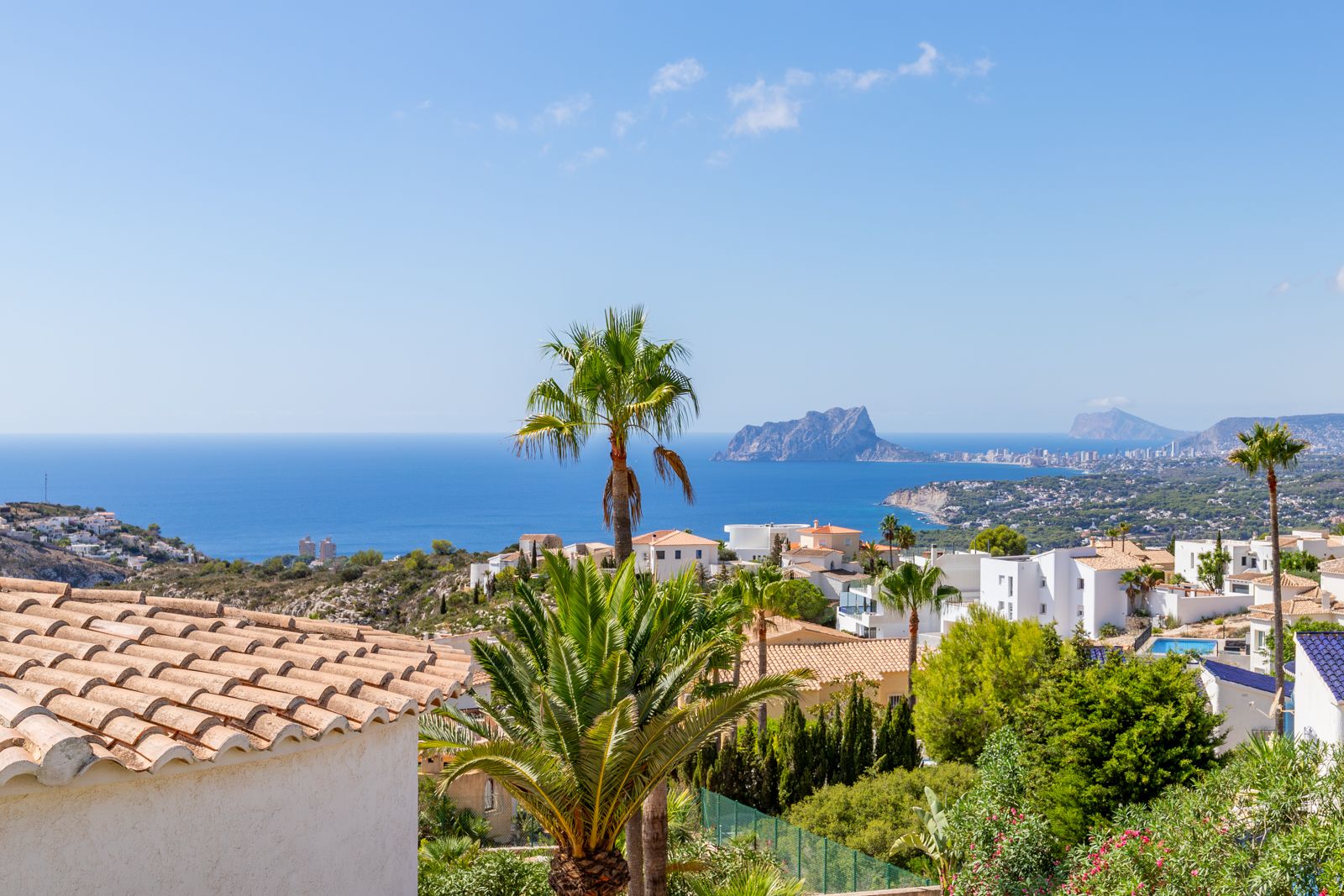 Vue panoramique sur la mer Méditerranée et le Peñón d'Ifach, mettant en valeur l'architecture côtière et la végétation locale de la Costa Blanca.