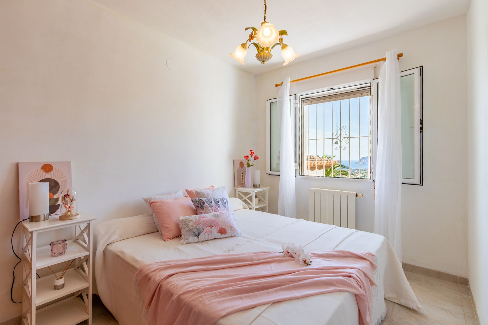 Chambre lumineuse avec lit double, murs blancs et carrelage au sol. La fenêtre offre une vue dégagée sur la mer Méditerranée et le célèbre Peñón de Ifach.