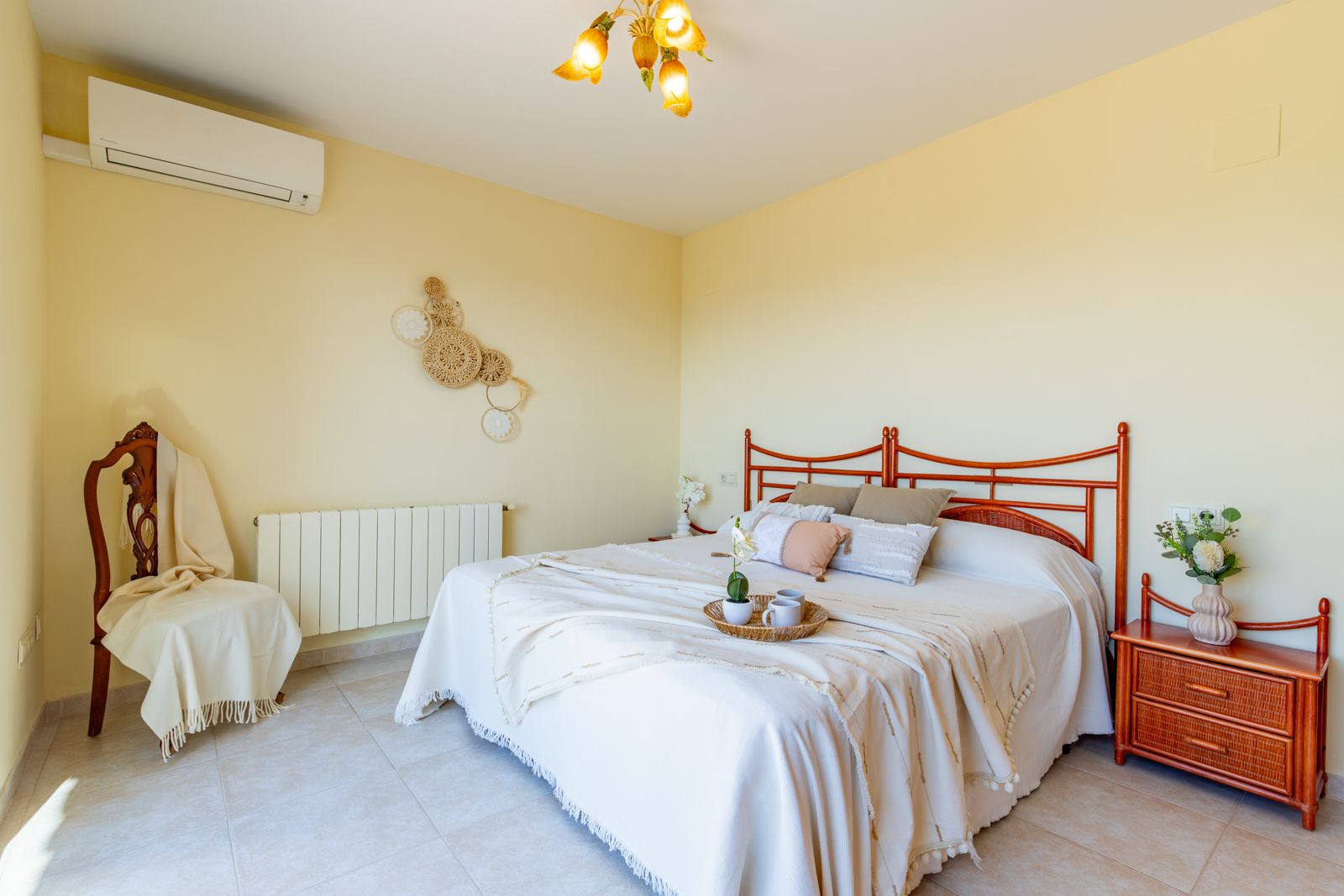 Chambre lumineuse avec lit double, tête de lit en bois sculpté, table de chevet assortie, climatisation réversible, radiateur et sol en grès cérame.