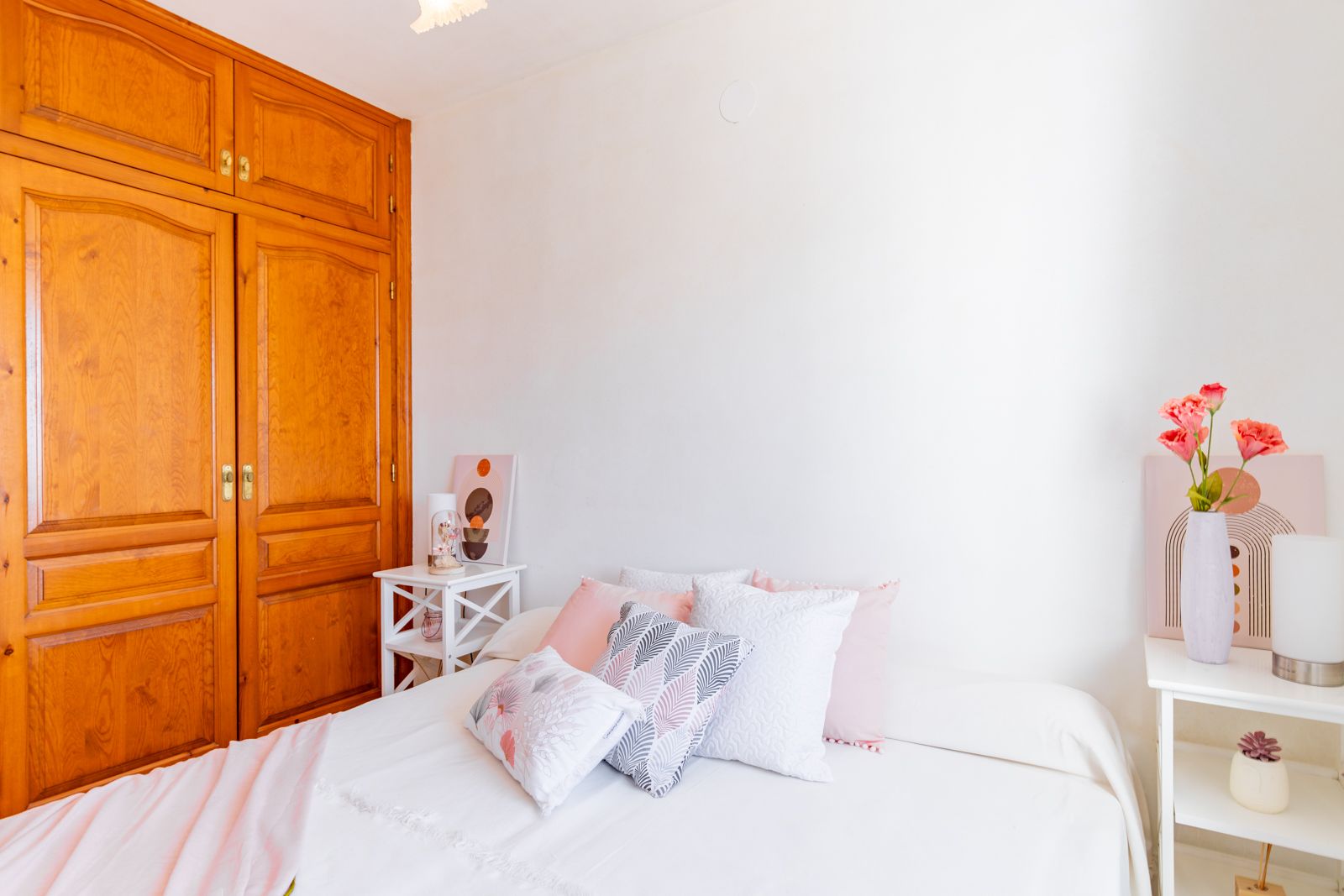 Chambre lumineuse dotée d'une grande armoire encastrée en bois massif, de murs blancs et de tables de chevet épurées créant une atmosphère sereine.