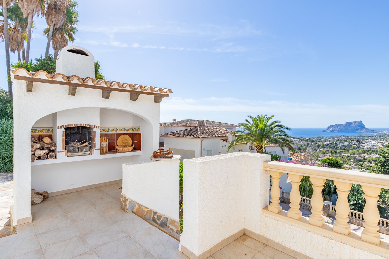 Espace barbecue maçonné avec cheminée et détails en céramique sur une terrasse surélevée, offrant une vue panoramique sur la mer et le Peñón de Ifach.