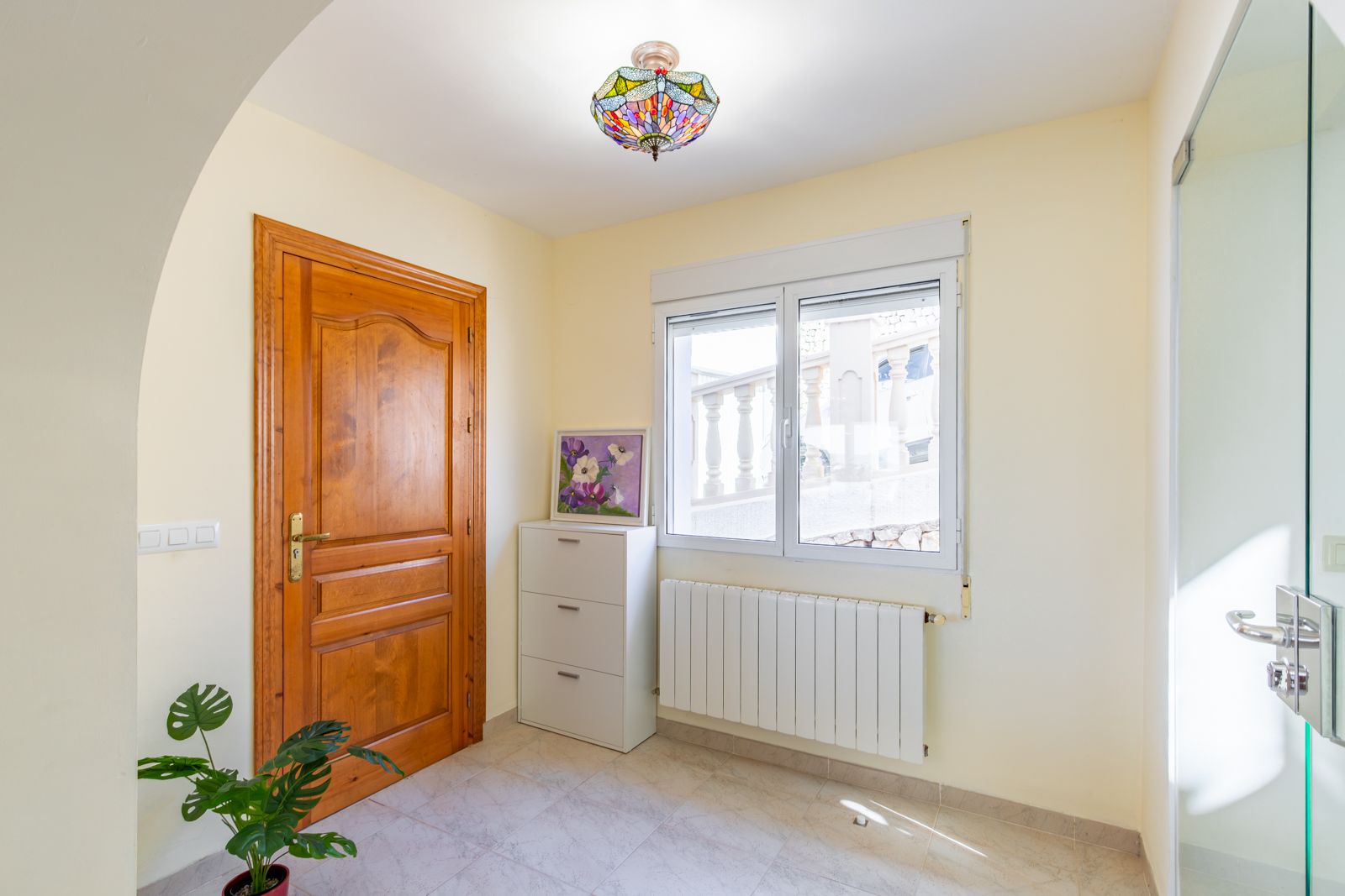 Hall d'entrée avec porte en bois massif, radiateur de chauffage central et plafonnier de style Tiffany, offrant un espace lumineux avec un sol en grès cérame.