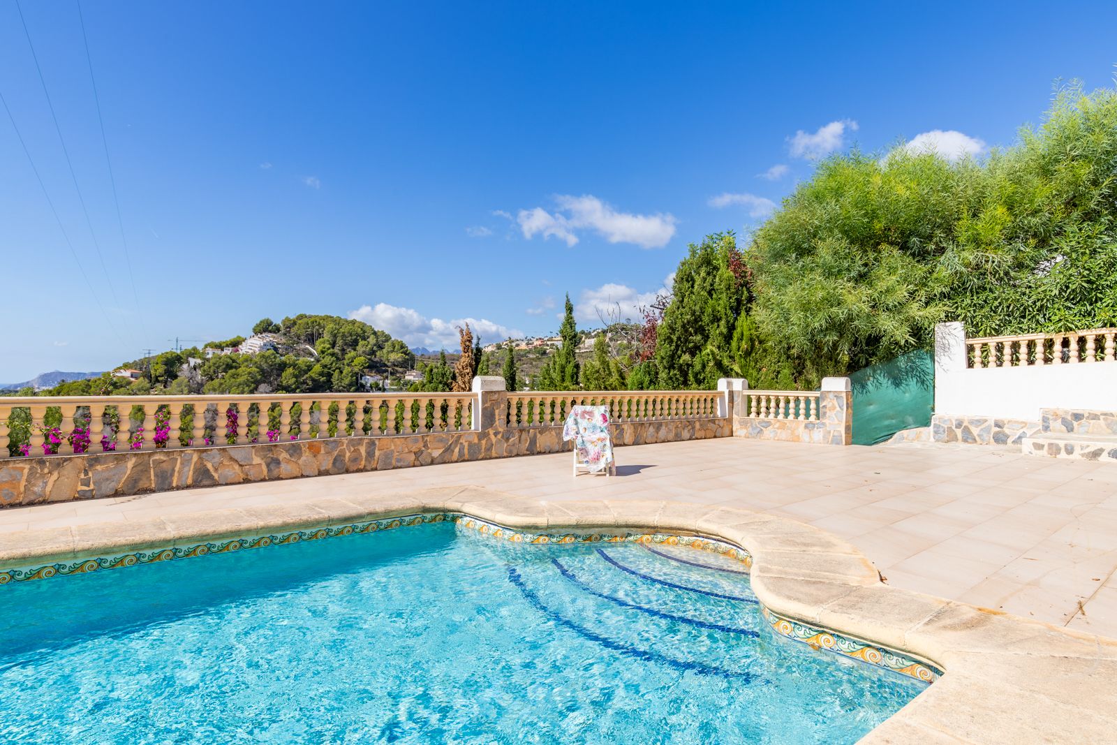 Piscine privée avec bordures en céramique décorative et grande terrasse ensoleillée, bordée d'une balustrade en pierre naturelle offrant une vue sur les collines.