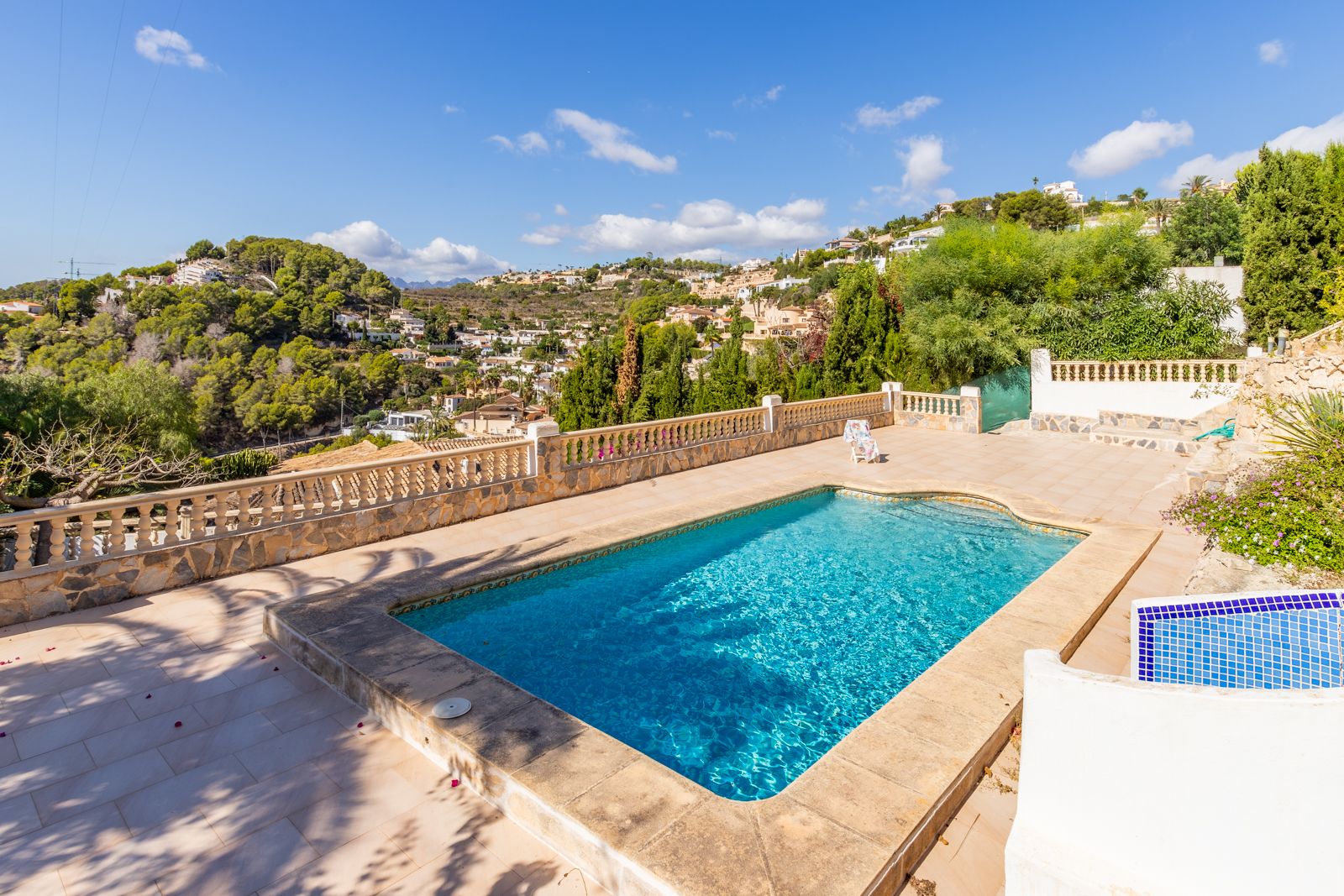 Piscine privée rectangulaire entourée d'une terrasse en pierre avec balustrade classique, offrant une vue panoramique sur les collines verdoyantes de Benimeit.