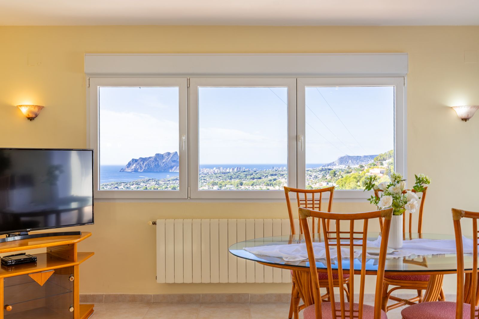 Salle à manger lumineuse avec de grandes fenêtres offrant une vue panoramique sur la mer et le Peñón de Ifach. Comprend un radiateur de chauffage central.