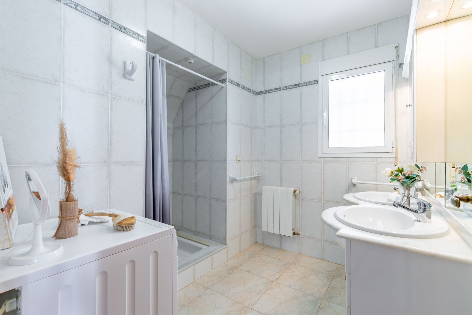 Salle de bain fonctionnelle avec double vasque en marbre, espace buanderie, douche à l'italienne et radiateur, éclairée par une fenêtre naturelle.