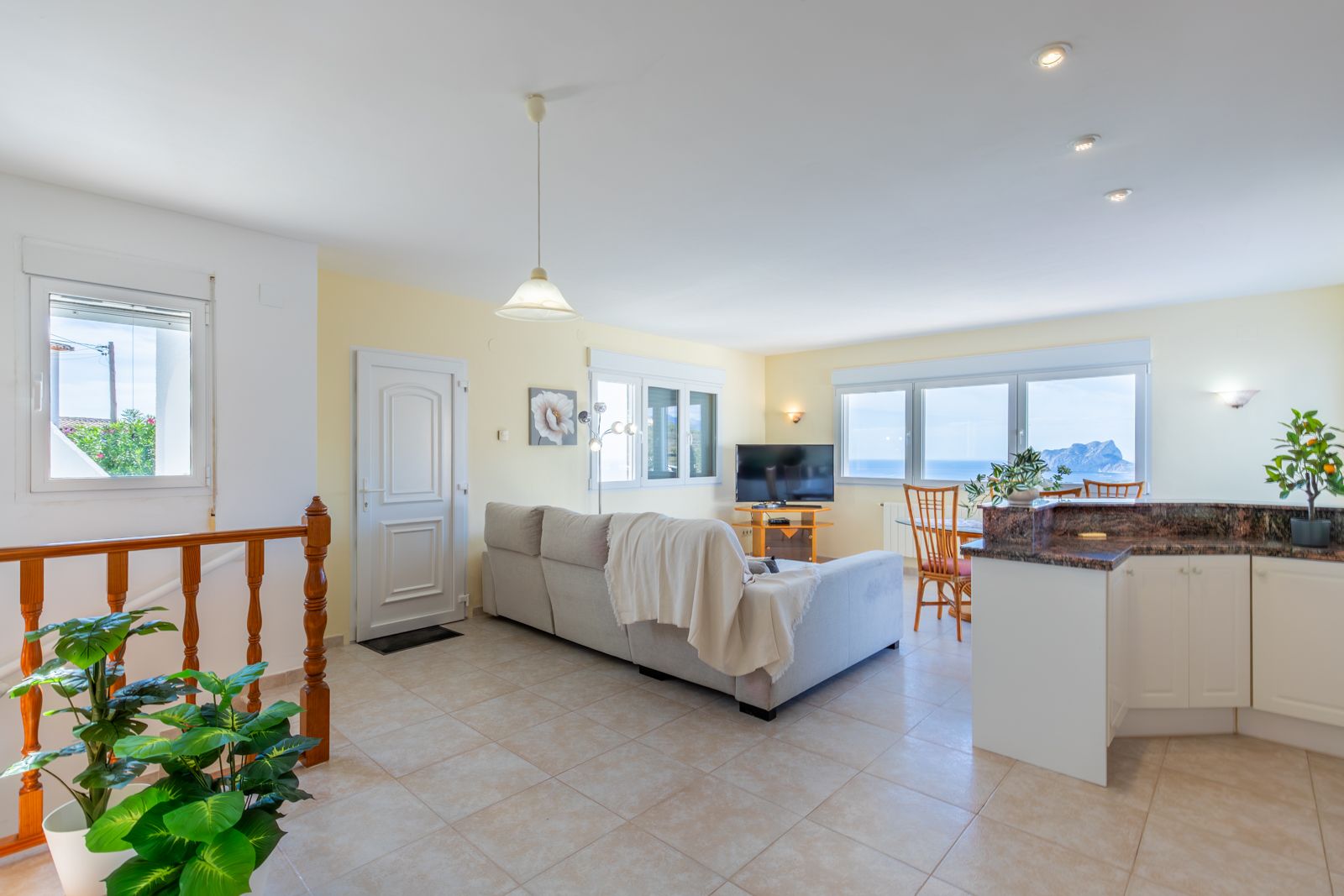 Salon et salle à manger à aire ouverte avec cuisine intégrée, plans de travail en granit et larges fenêtres offrant une vue sur la mer et le Peñón de Ifach.