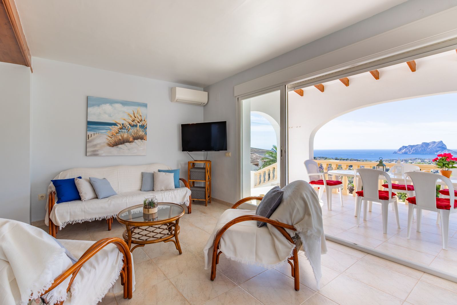 Salon lumineux avec mobilier en rotin ouvrant sur une terrasse couverte. Profitez d'une vue panoramique sur la mer Méditerranée et le célèbre Peñón de Ifach.