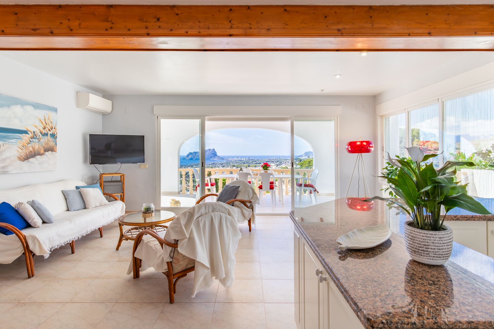 Salon lumineux avec poutres en bois apparentes, cuisine ouverte avec plan de travail en granit et terrasse offrant une vue panoramique sur la mer et le Peñón de Ifach.