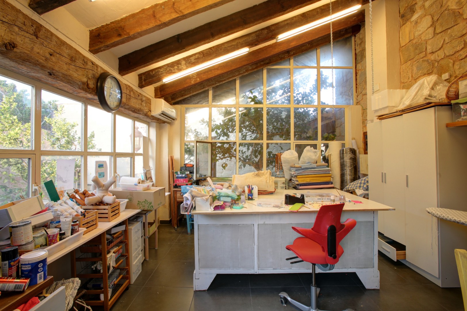 Atelier de création avec poutres en bois massif, murs en pierre apparente et grandes baies vitrées offrant une luminosité optimale.