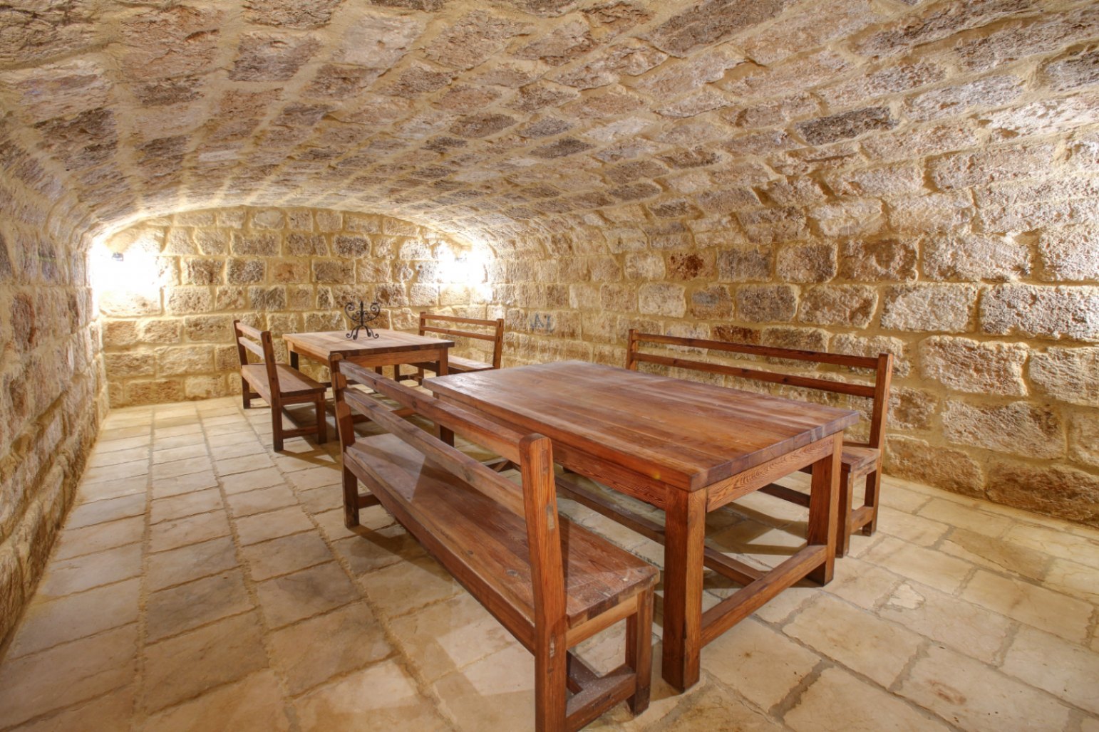 Cave à vin voûtée en pierre naturelle avec tables et bancs en bois massif, sol en dalles de pierre et éclairage d'ambiance chaleureux.