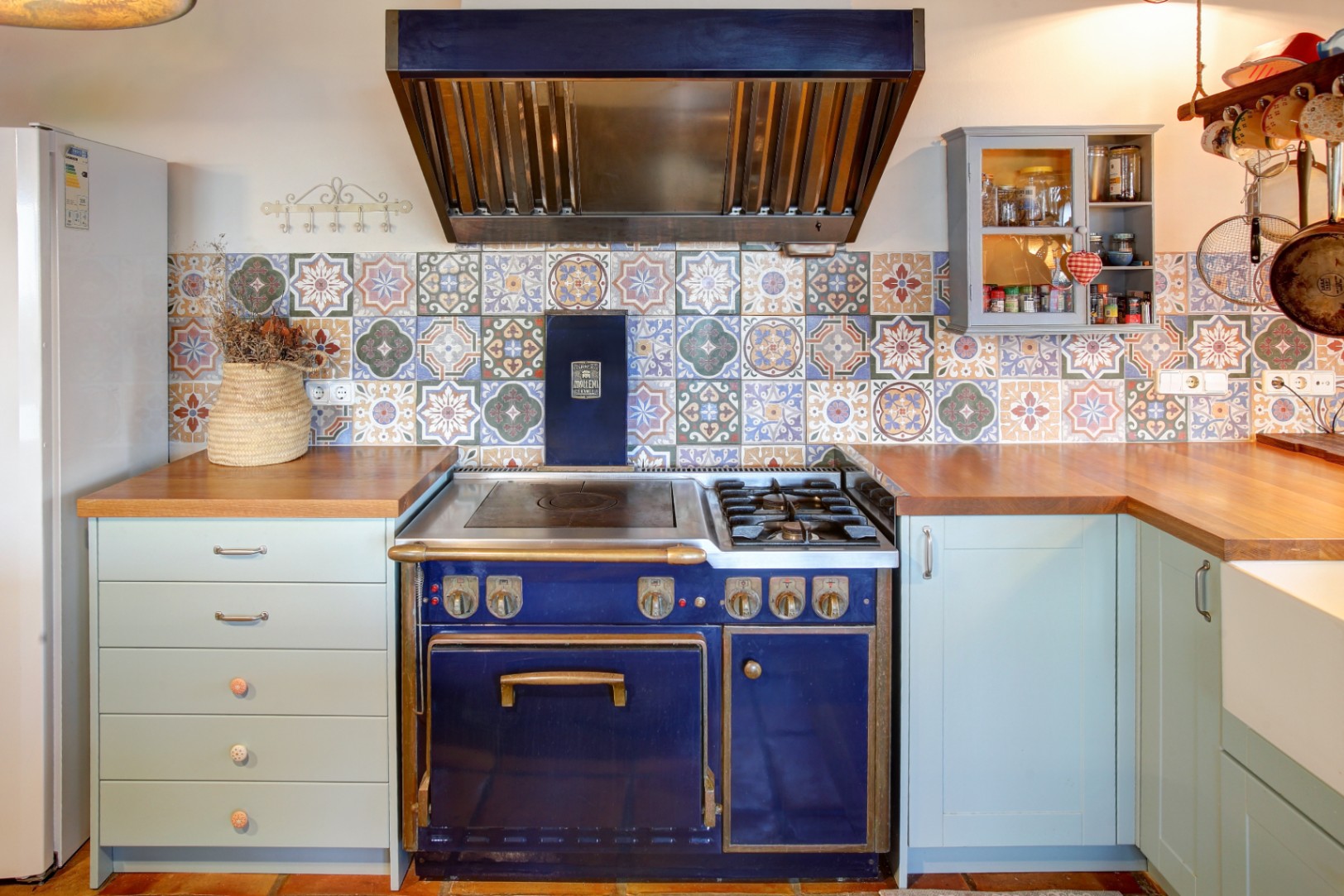 Cuisinière professionnelle Molteni bleu cobalt avec finitions en laiton, entourée de plans de travail en bois et d'une crédence en carreaux de ciment à motifs.