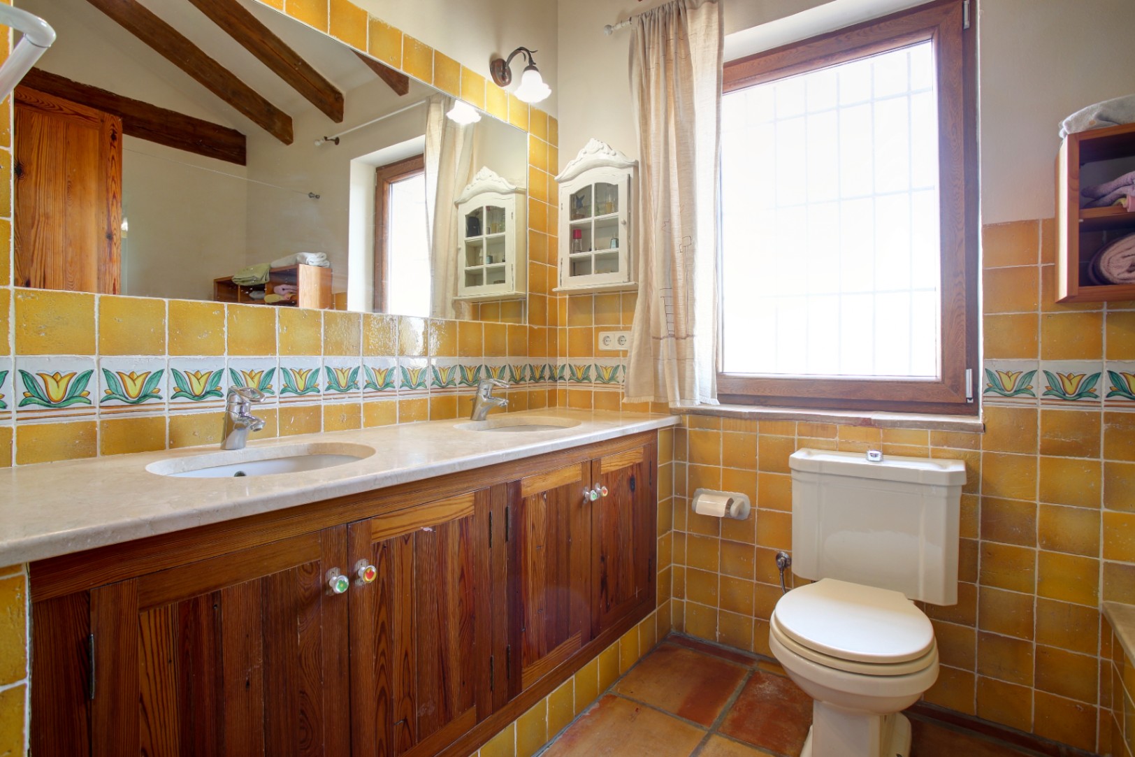Salle de bain rustique avec double vasque en marbre, meubles en bois de mobila et carreaux moutarde. Poutres en bois apparentes et sol en terre cuite traditionnelle.