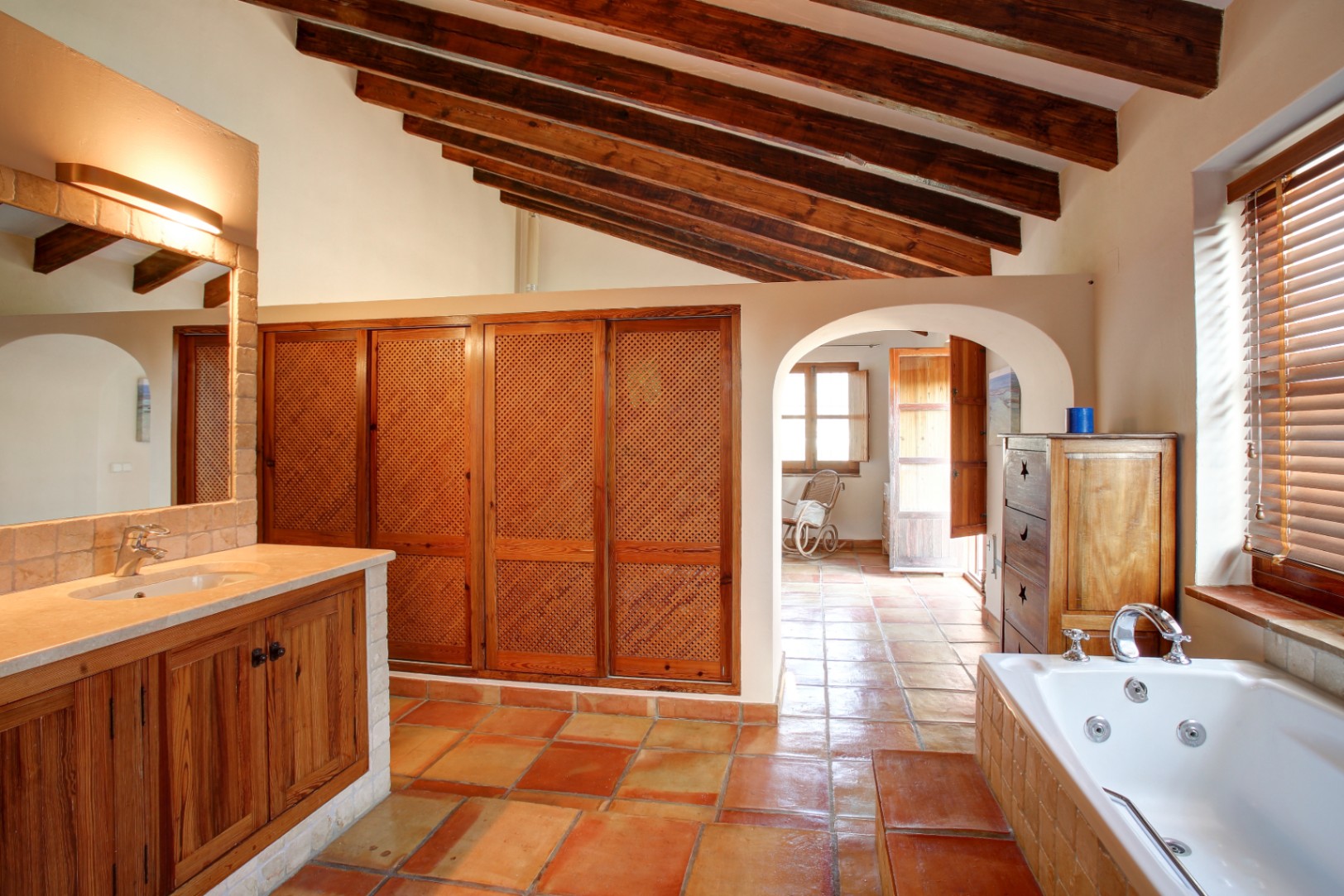 Salle de bains rustique avec poutres apparentes, sol en terre cuite et baignoire balnéo. Comprend des placards en bois ajouré et un plan de toilette en marbre.