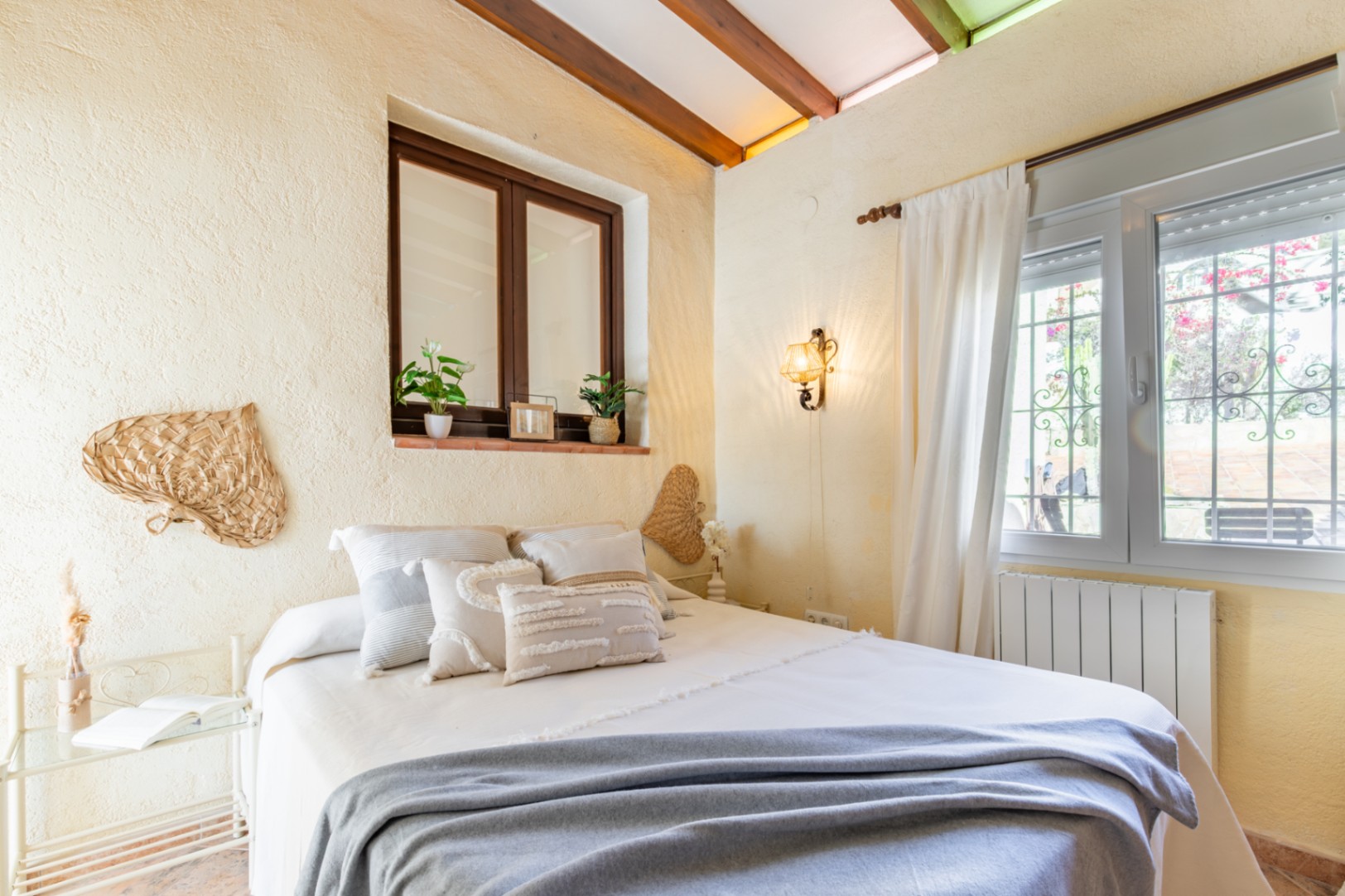 Chambre avec poutres en bois apparentes, murs texturés et double fenêtrage. L'espace est décoré dans un style méditerranéen avec un éclairage chaleureux.
