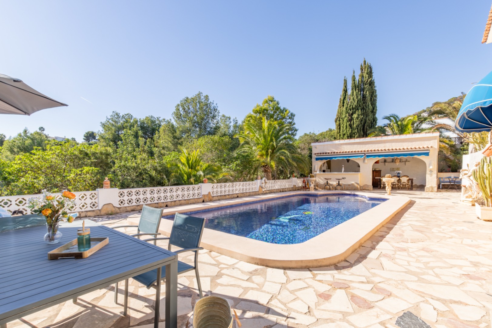 Espace extérieur avec piscine de 42 m², terrasse en pierre naturelle et cuisine d'été couverte, entouré d'une végétation dense et de vues dégagées.